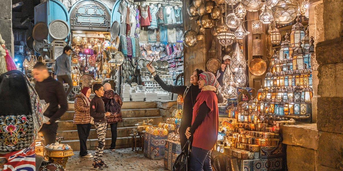 Shoppers browse glowing ornate lanterns and metalwork at a bustling Cairo bazaar stall.