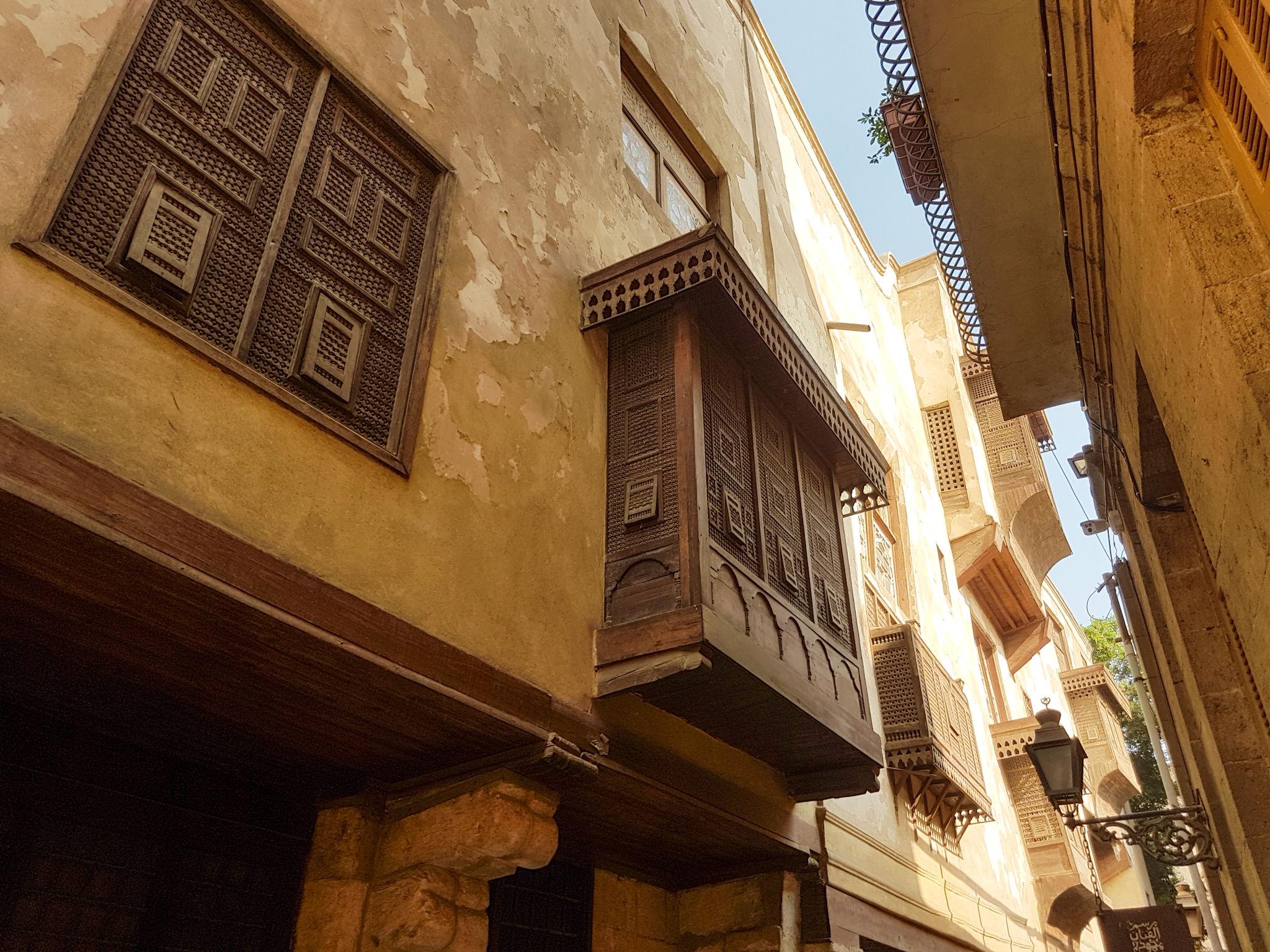 Ornate carved wooden mashrabiya balconies projecting over a narrow historic Cairo alleyway