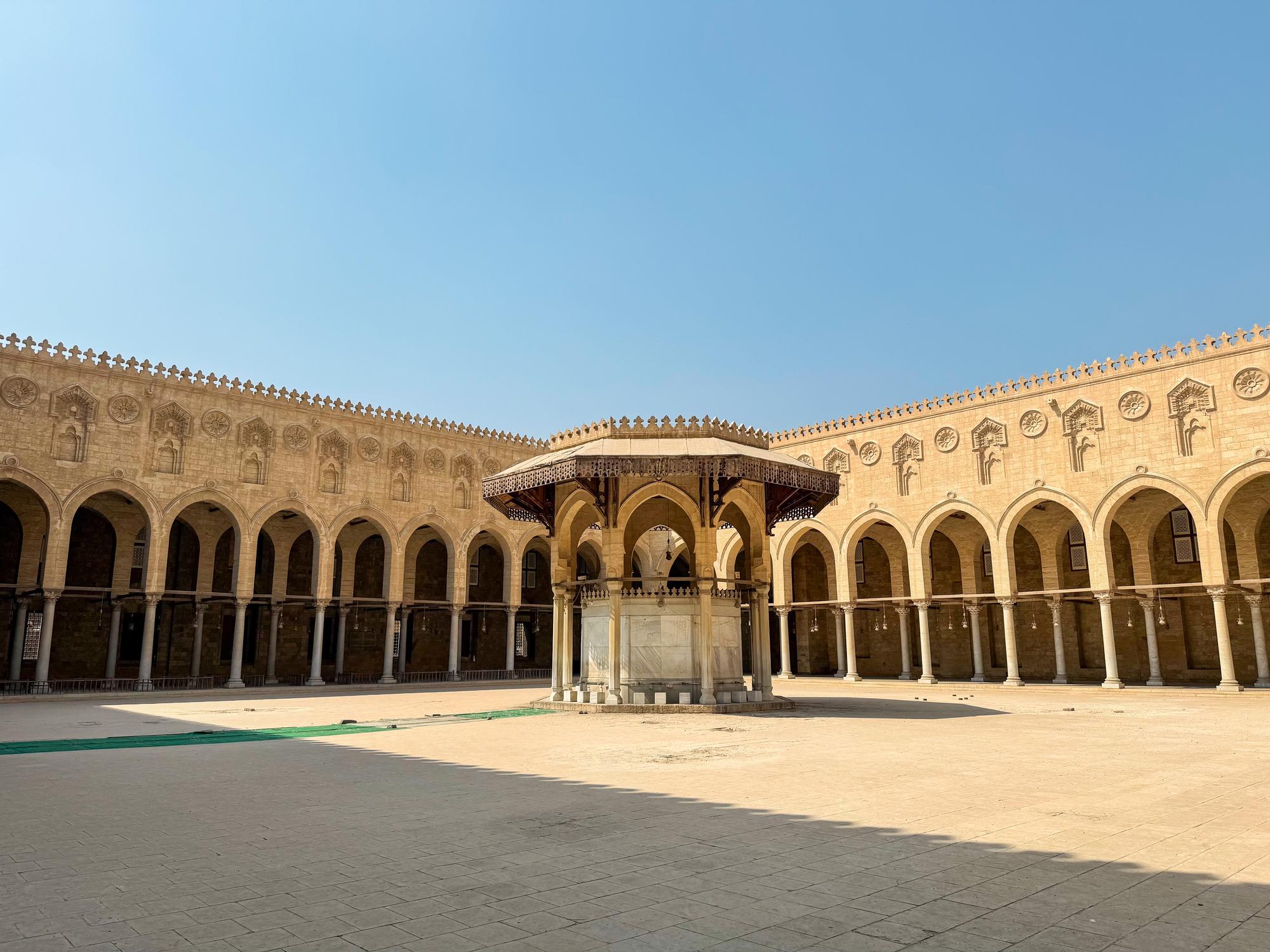 Sun-lit open courtyard with a central ablution fountain surrounded by arched colonnades