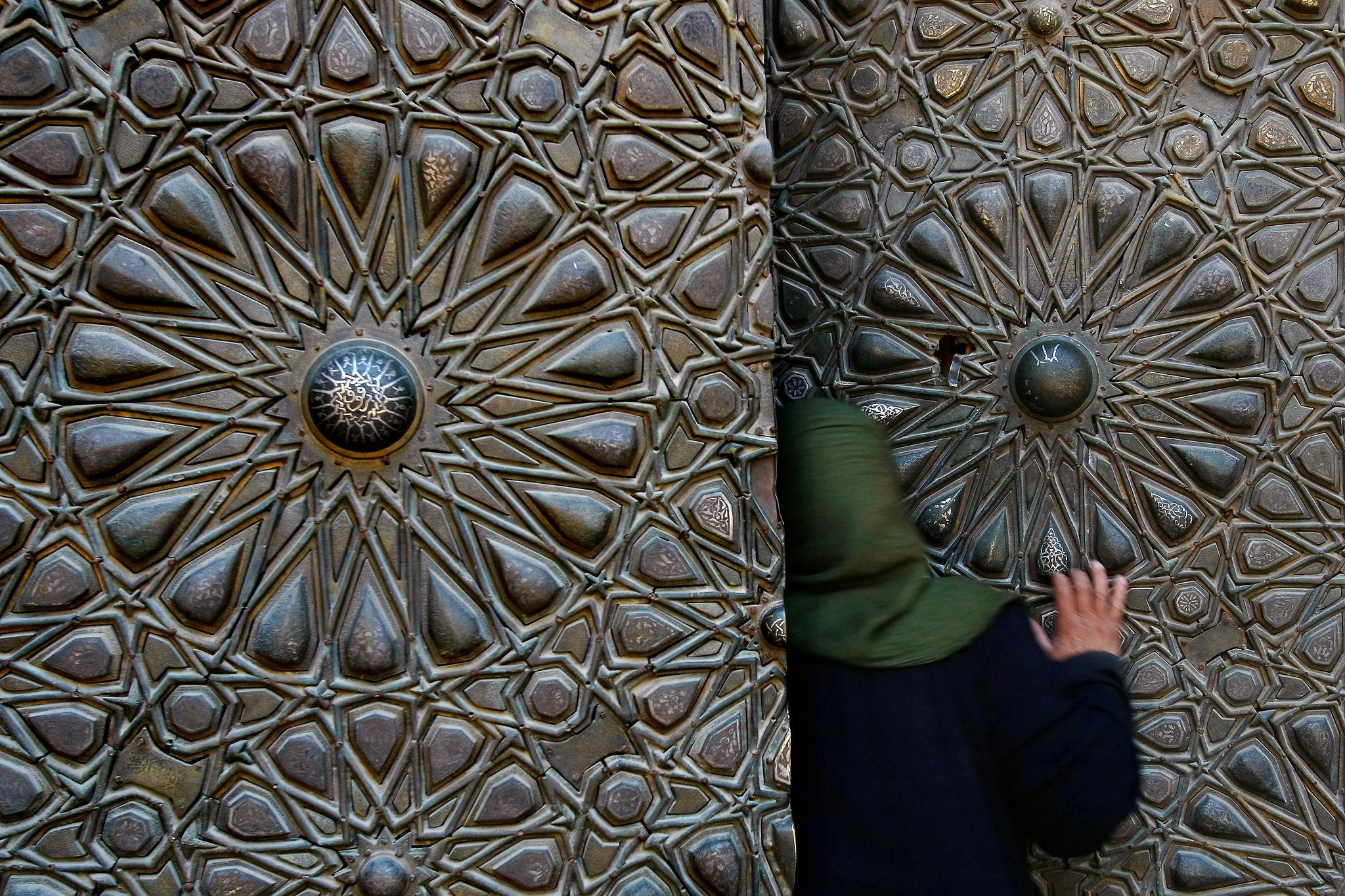 A person slipping through the massive ornately patterned bronze doors of the NMEC