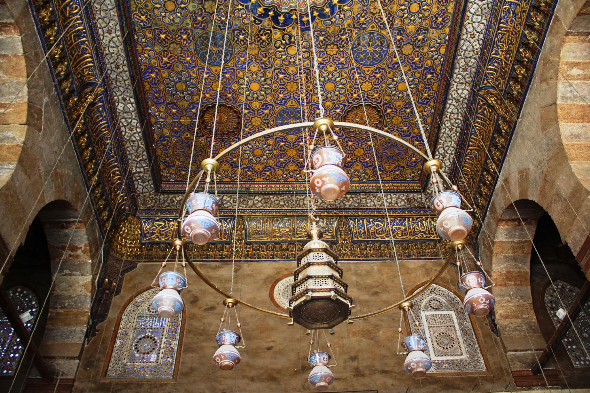 Elaborate brass chandelier with ceramic bowls beneath a gilded Islamic patterned ceiling at NMEC