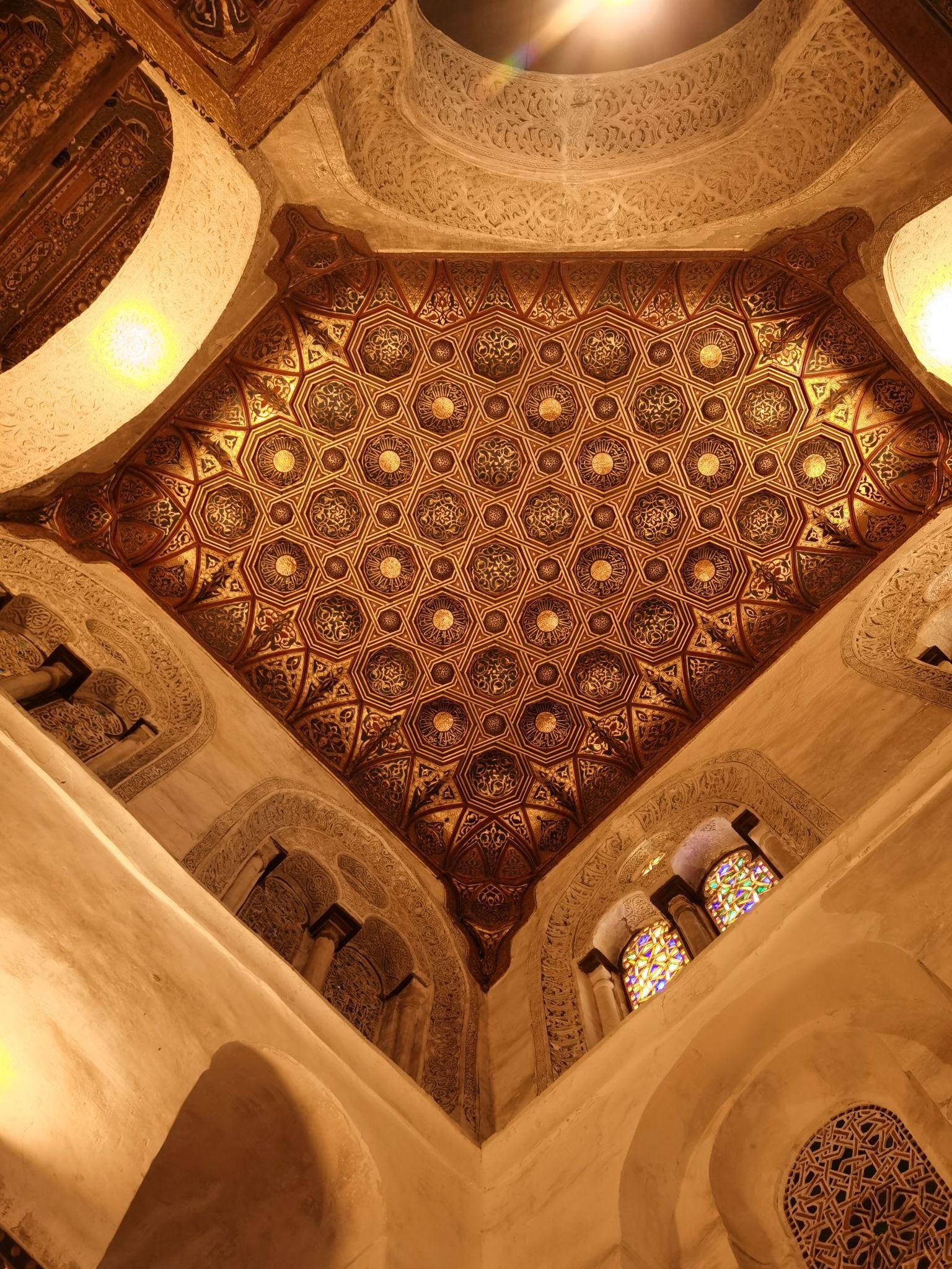 Upward view of an intricately carved golden geometric ceiling with Moorish star patterns at NMEC