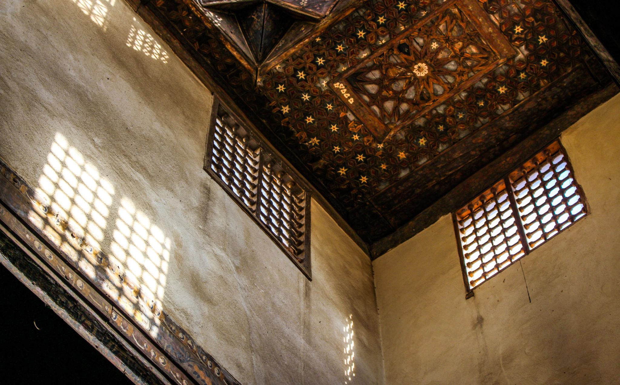 Intricate carved wooden ceiling with star patterns and mashrabiya windows casting geometric light