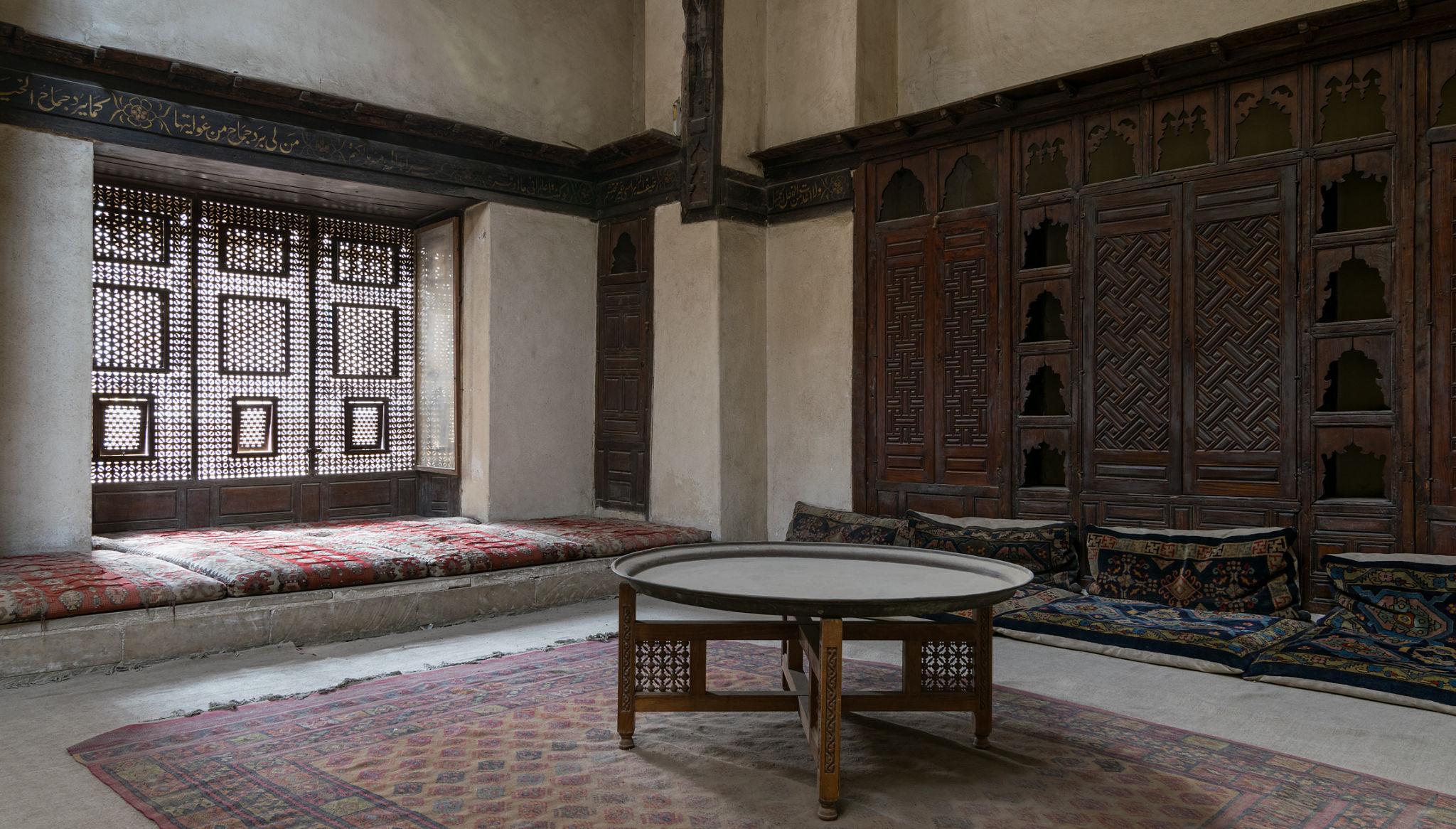 Historic Egyptian reception room with carved mashrabiya screens, low cushioned seating, and ornate wooden panels