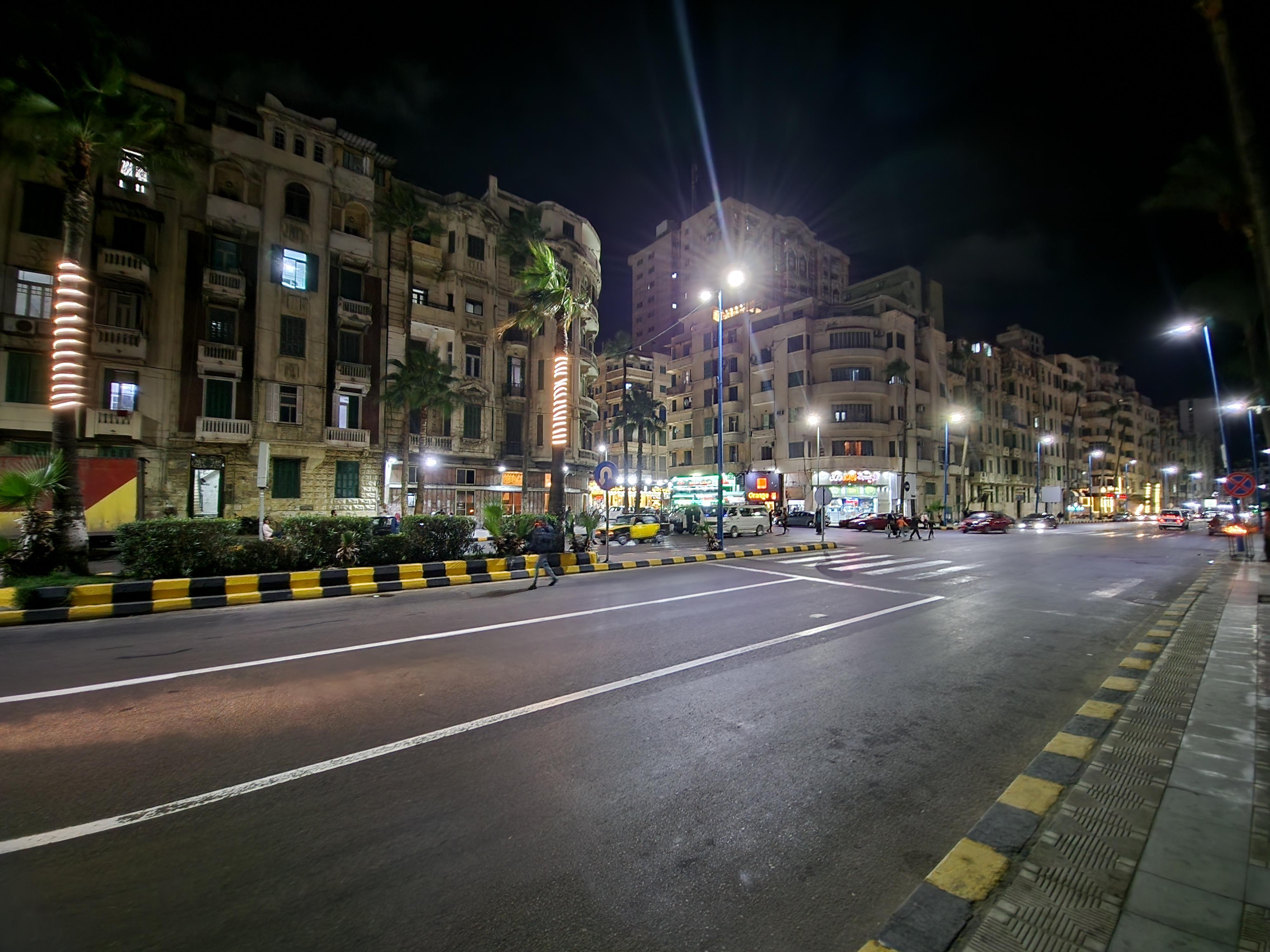 Nighttime view of Alexandria Corniche street with lit historic apartment buildings and palm trees