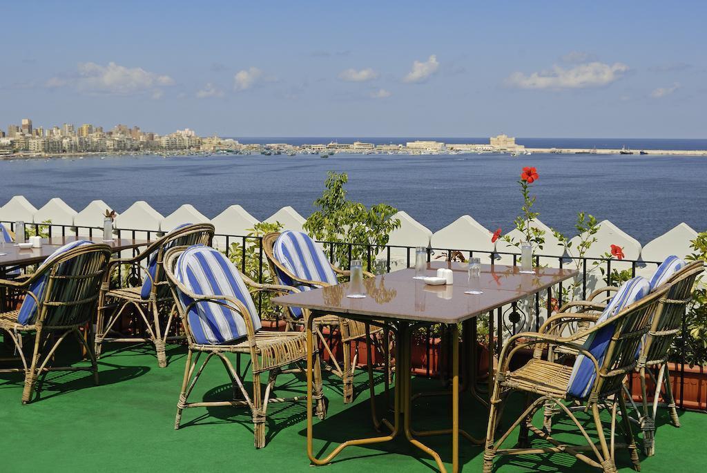 Cafe terrace with striped chairs overlooking Alexandria's Eastern Harbor and Qaitbay fortress skyline