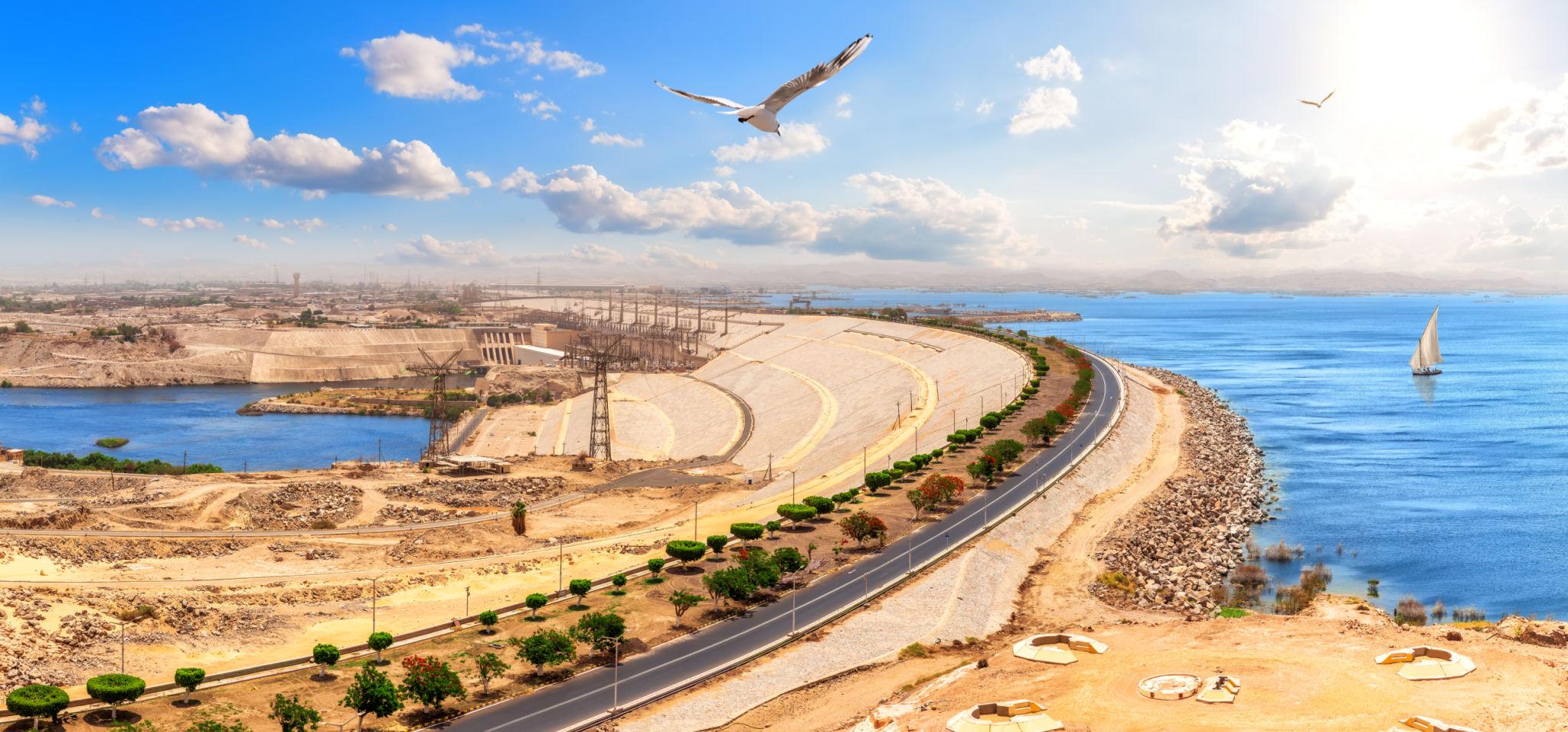 Panoramic view of Aswan High Dam curving between Lake Nasser and the Nile with felucca sailing