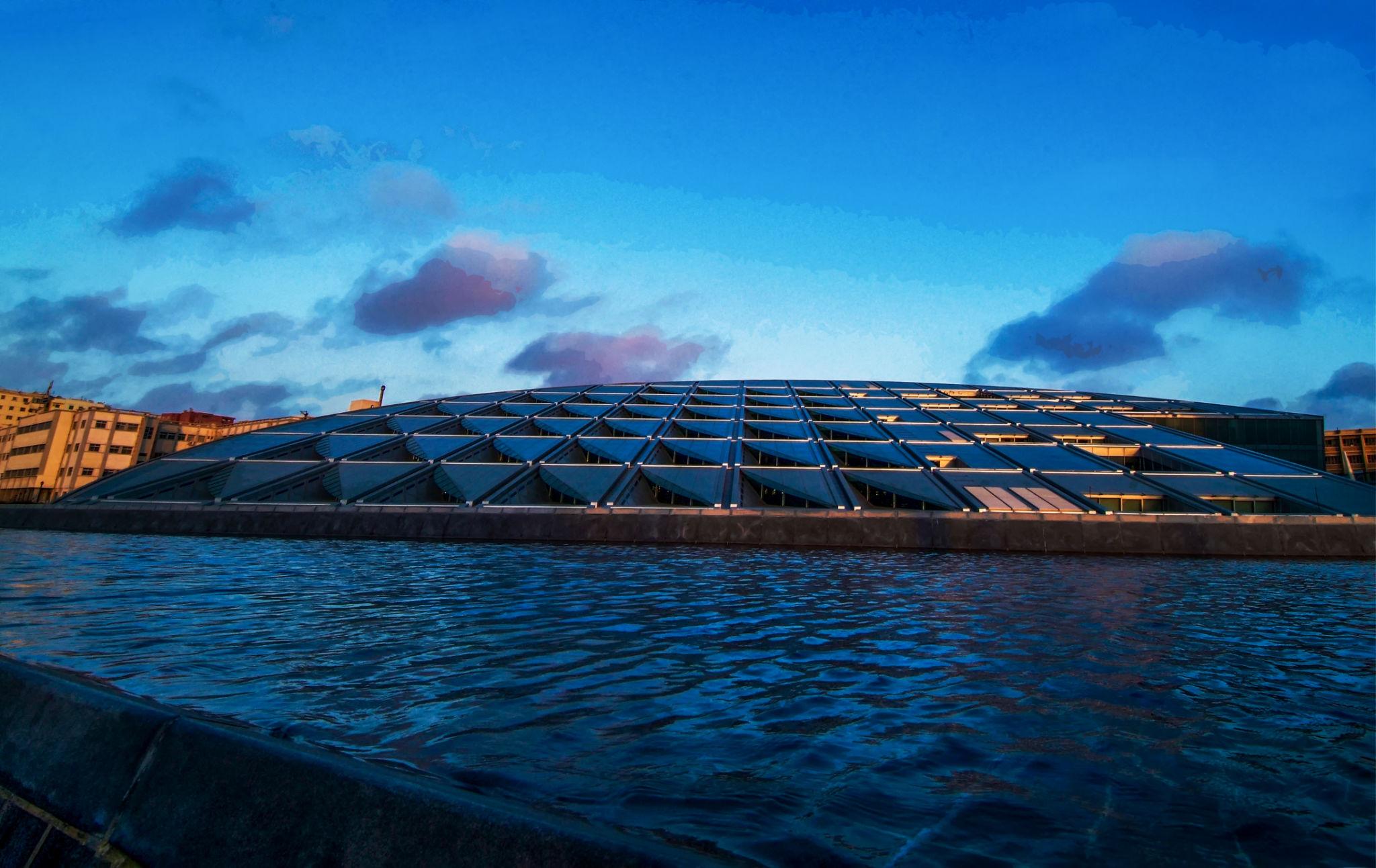 Bibliotheca Alexandrina's tilted glass and steel disc roof at dusk above the harbor