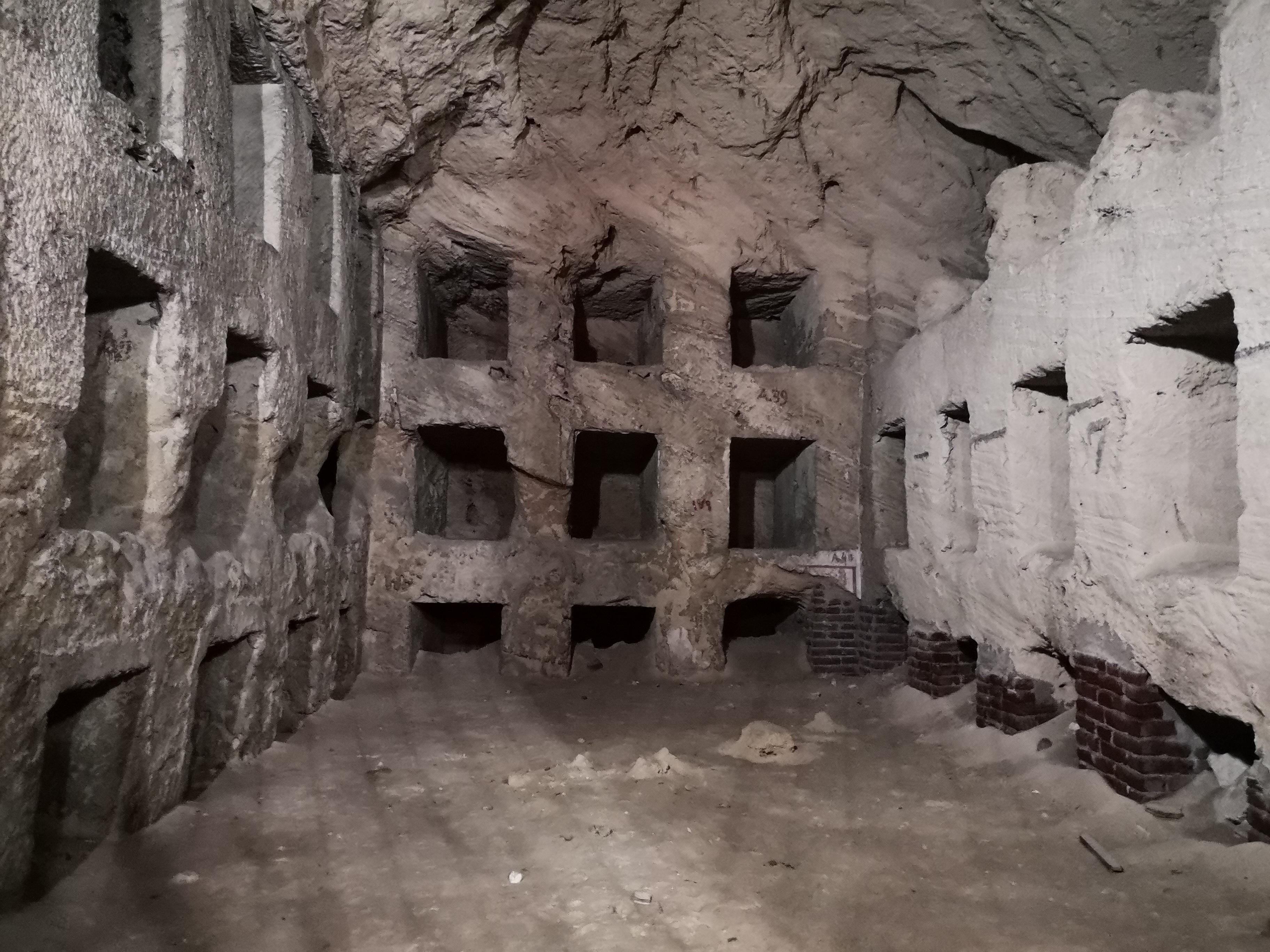 Rows of rock-cut loculi burial niches stacked along catacomb gallery walls