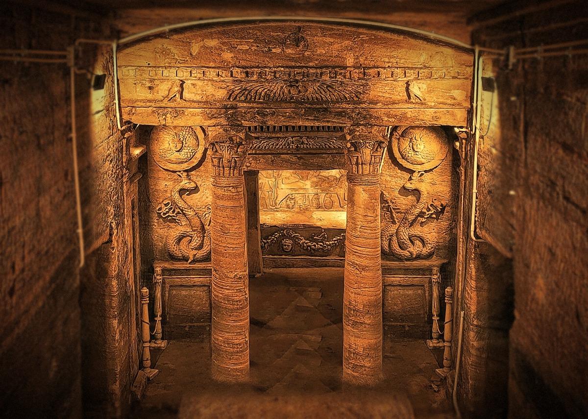 Ornate main tomb facade with columns, winged sun disk and carved pediment at Kom el-Shoqafa