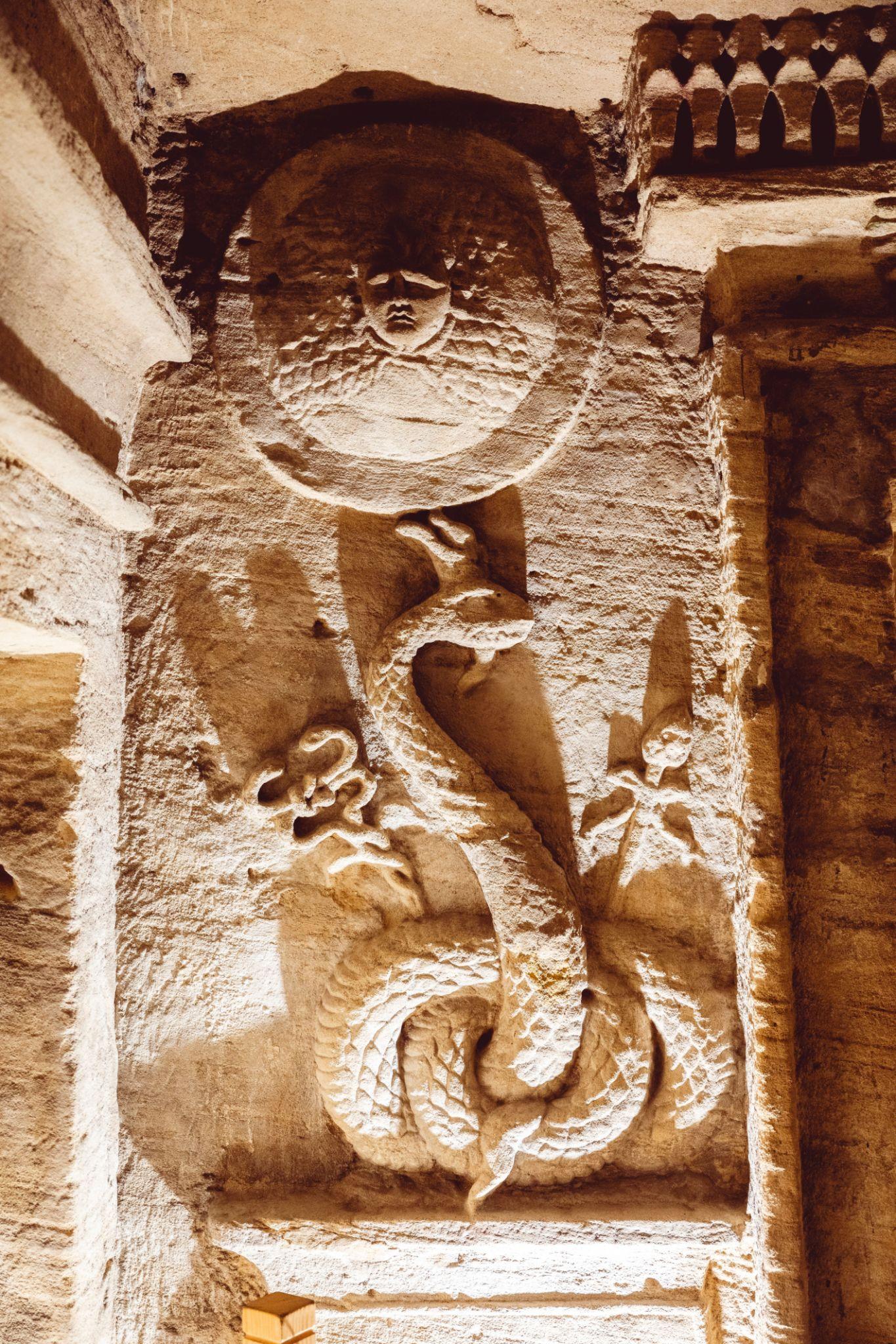 Carved Medusa shield above a coiled agathodaemon serpent relief guarding a tomb entrance