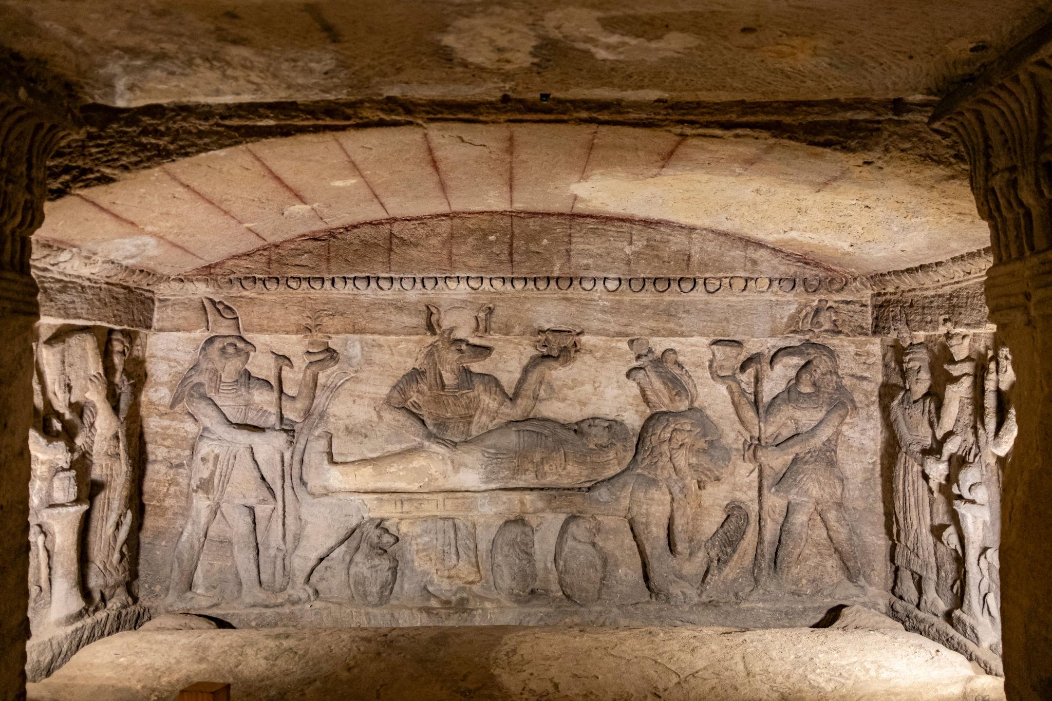 Carved sarcophagus frieze depicting Egyptian gods performing mummification rites on a reclining figure