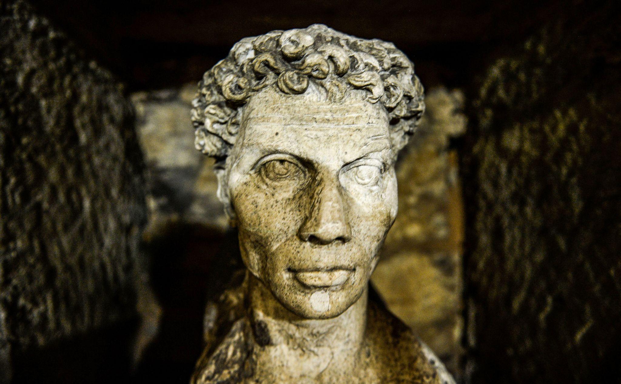 Weathered Greco-Roman marble portrait bust with curly hair inside the Alexandria catacombs