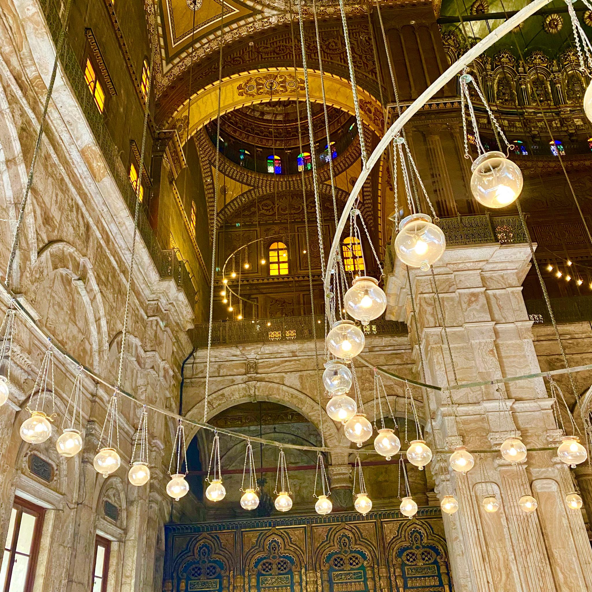 Rings of glass lamps hanging beneath the gilded arches of the Muhammad Ali Alabaster Mosque