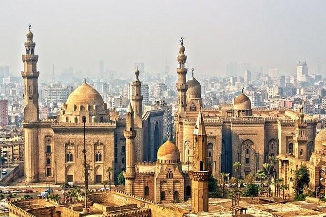Cluster of Mamluk mosque-mausoleum domes and minarets above Cairo with modern skyline behind
