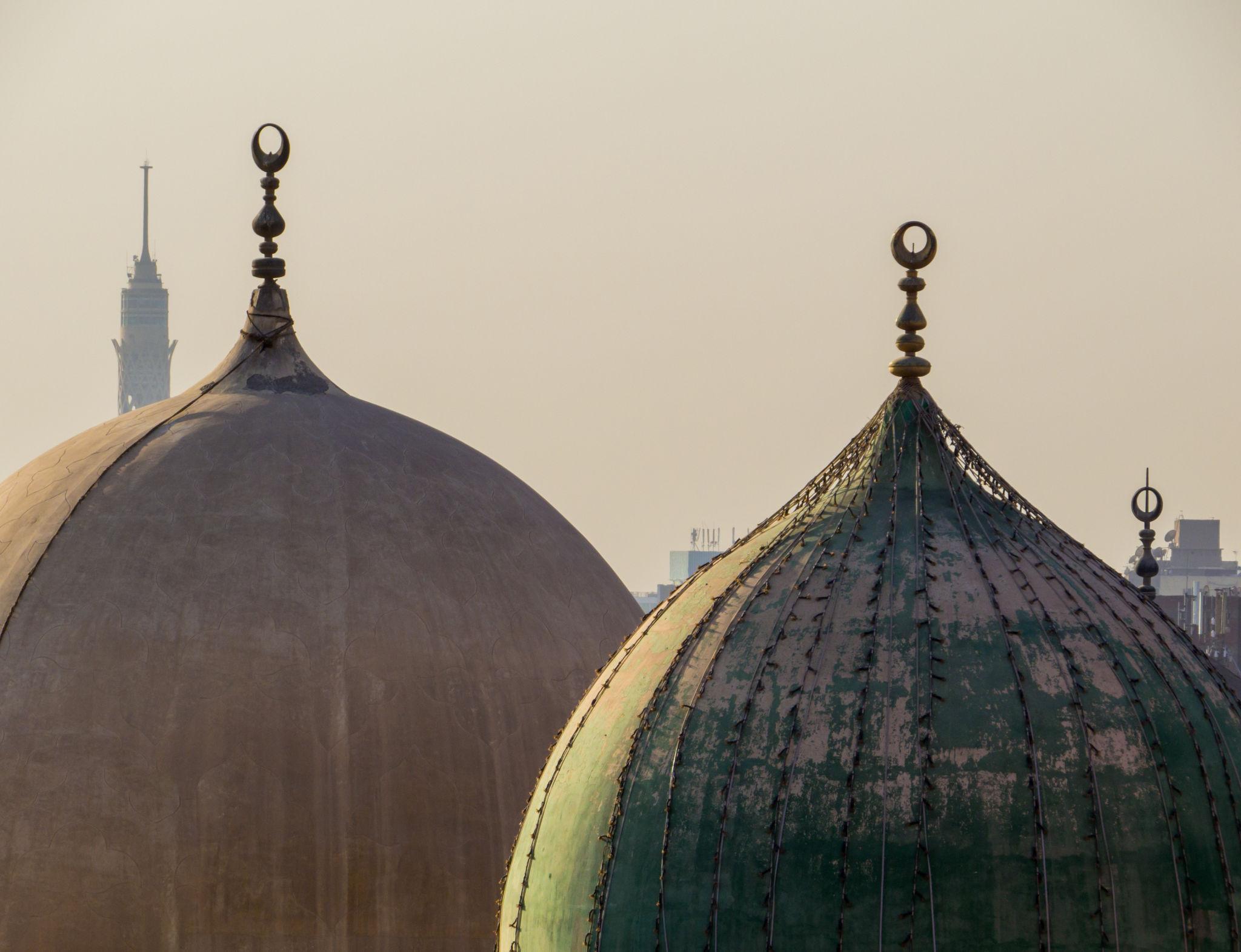 Two ribbed mausoleum domes crowned with crescent finials against hazy Cairo sky