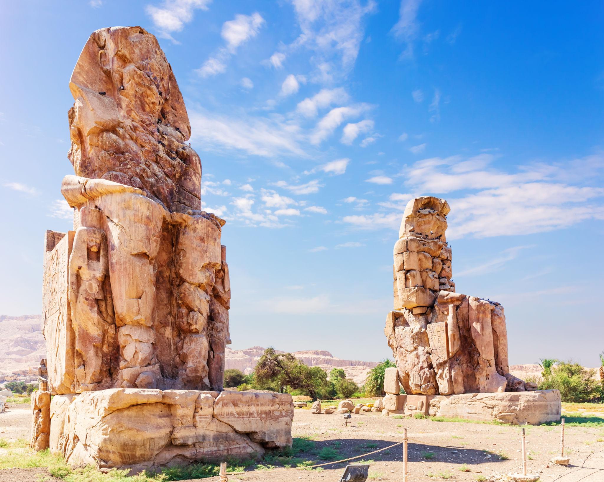 Both Colossi of Memnon statues standing under bright blue skies in Luxor
