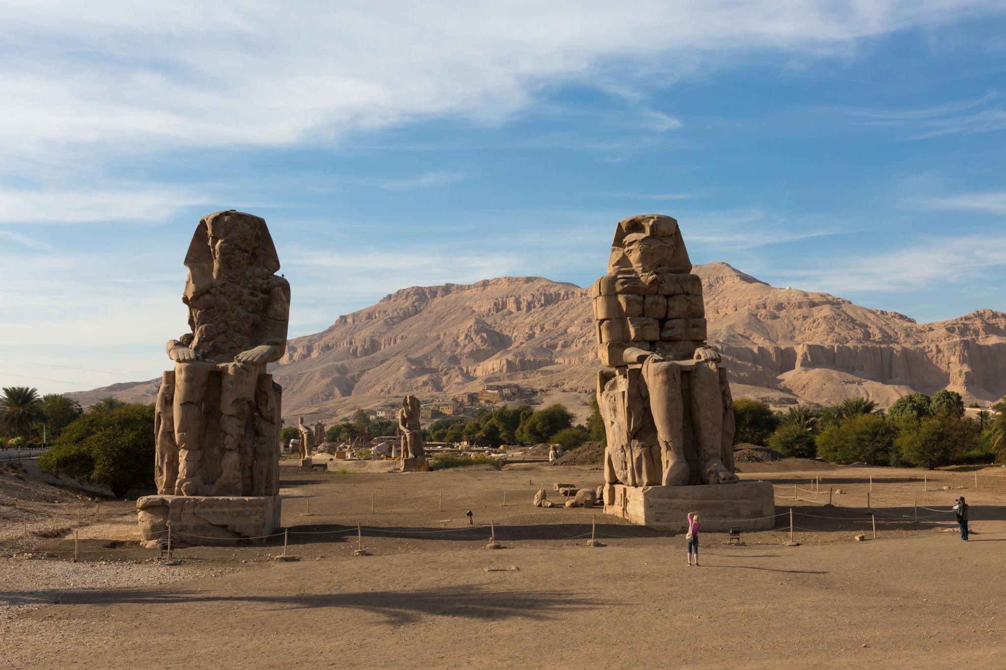 Colossi of Memnon with Theban mountains behind and a visitor dwarfed in the foreground