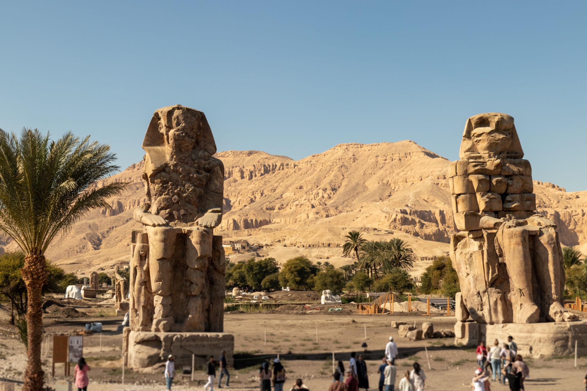 Tourists visit the Colossi of Memnon with Theban hills rising in the background