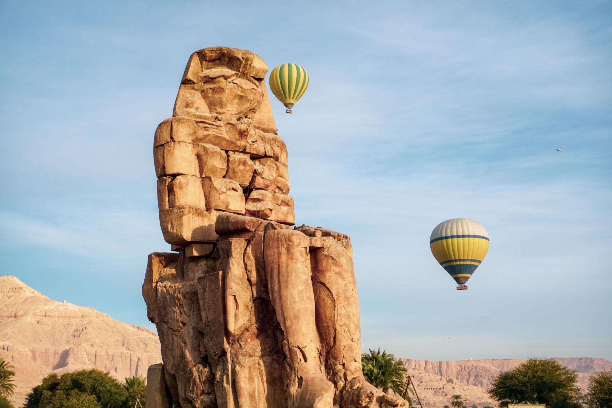 Hot air balloons float past a Colossus of Memnon at sunrise in Luxor, Egypt