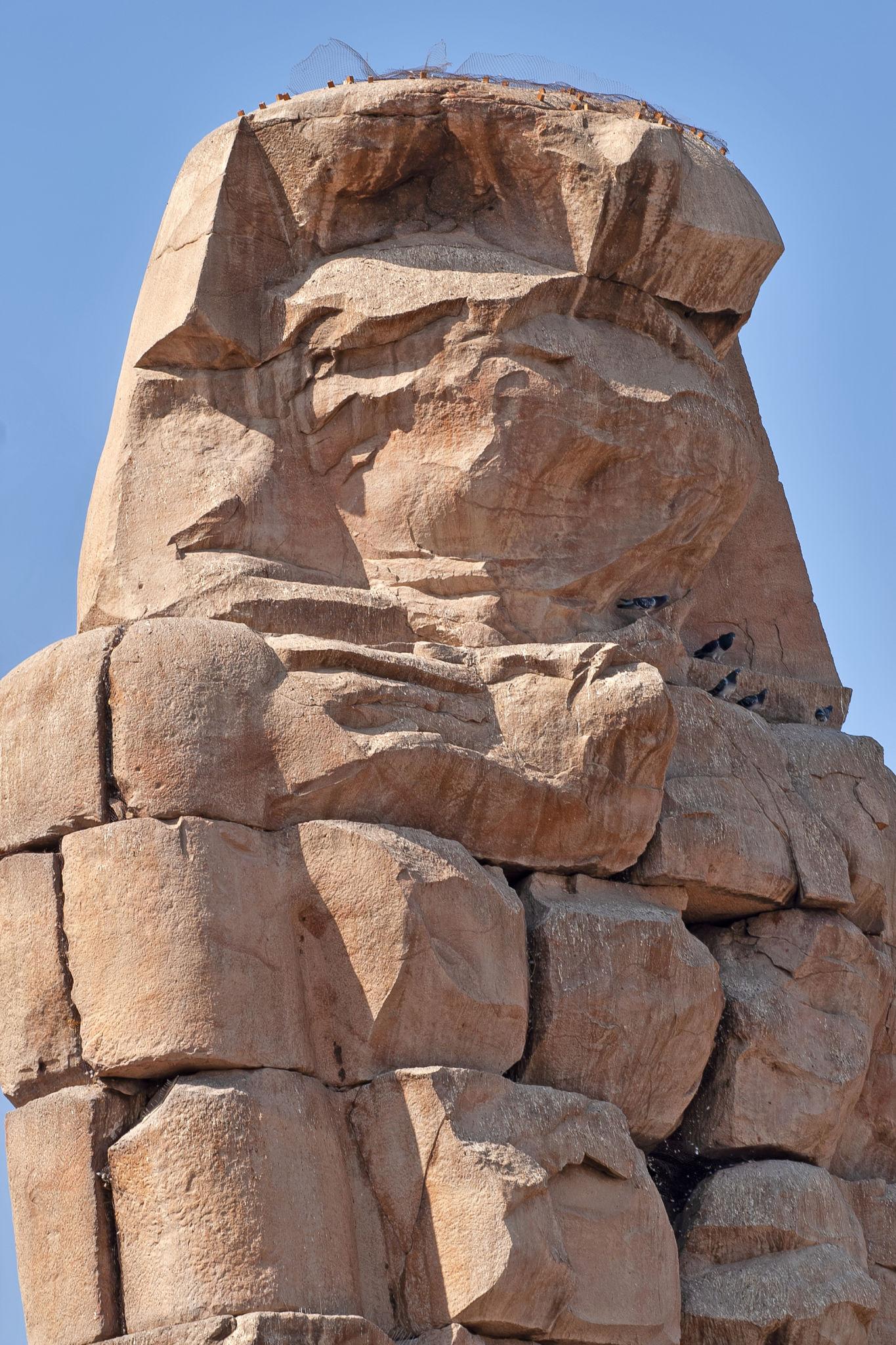 Close-up of a weathered Colossus of Memnon torso and arm against blue sky