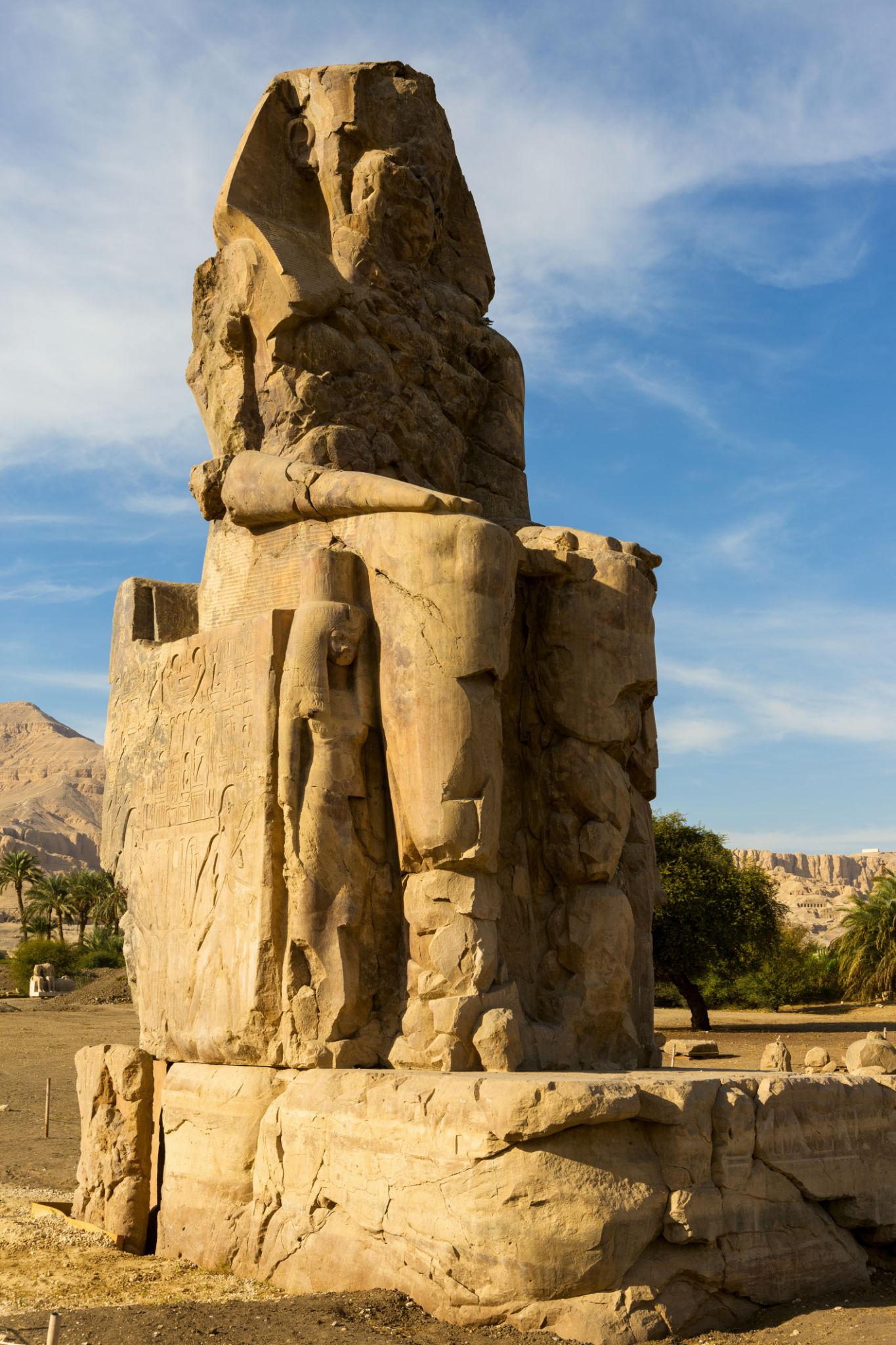 Tall vertical view of a single Colossus of Memnon with carved family figures at its side