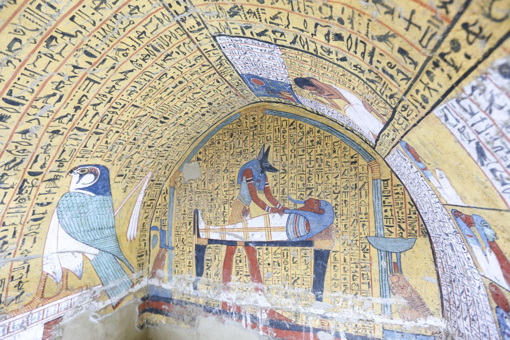 Tomb painting of Anubis tending a mummy on a bier framed by dense hieroglyphic columns