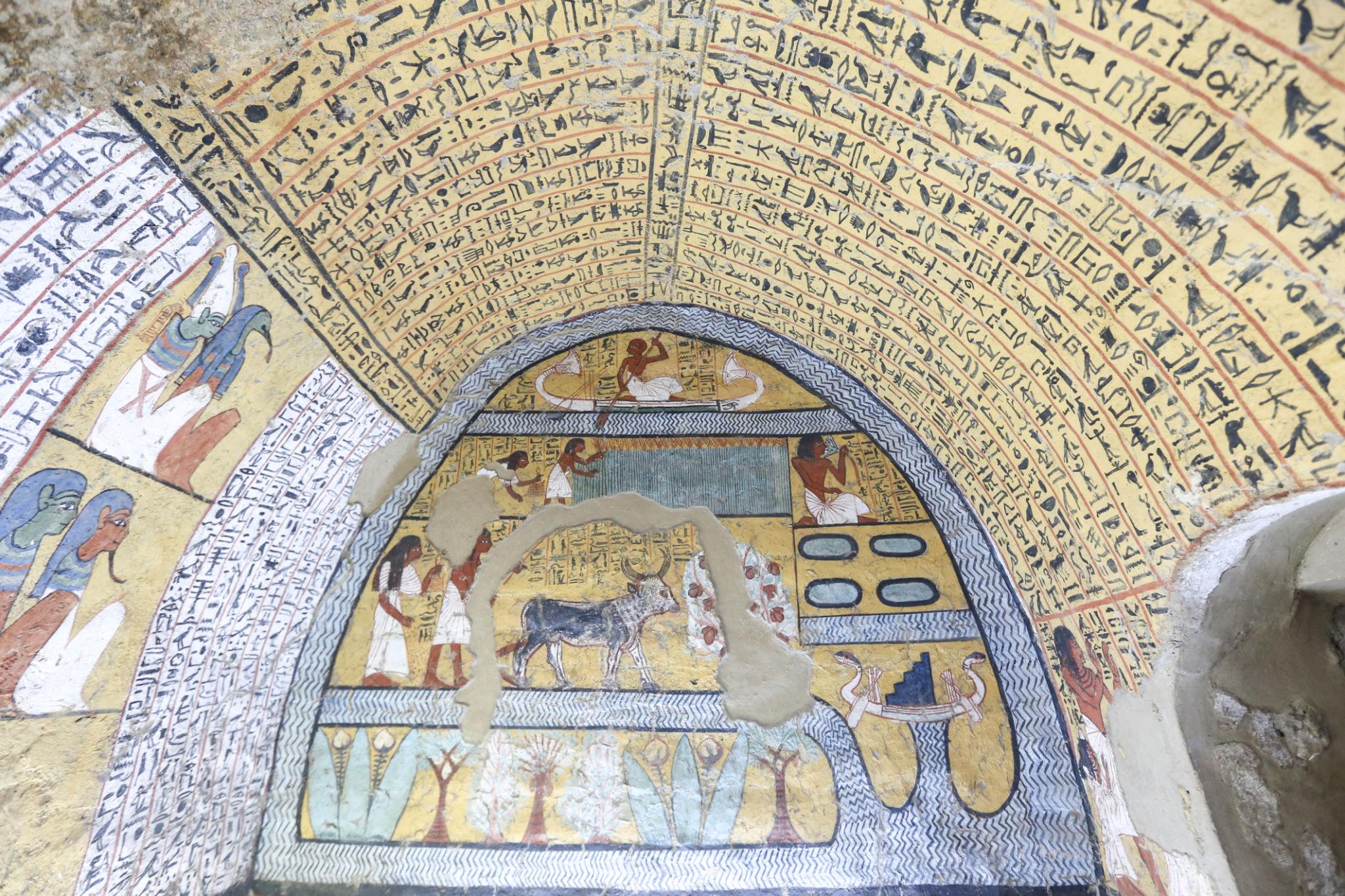 Richly painted vaulted burial chamber at Deir el-Medina with hieroglyph-filled ceiling and funerary scenes
