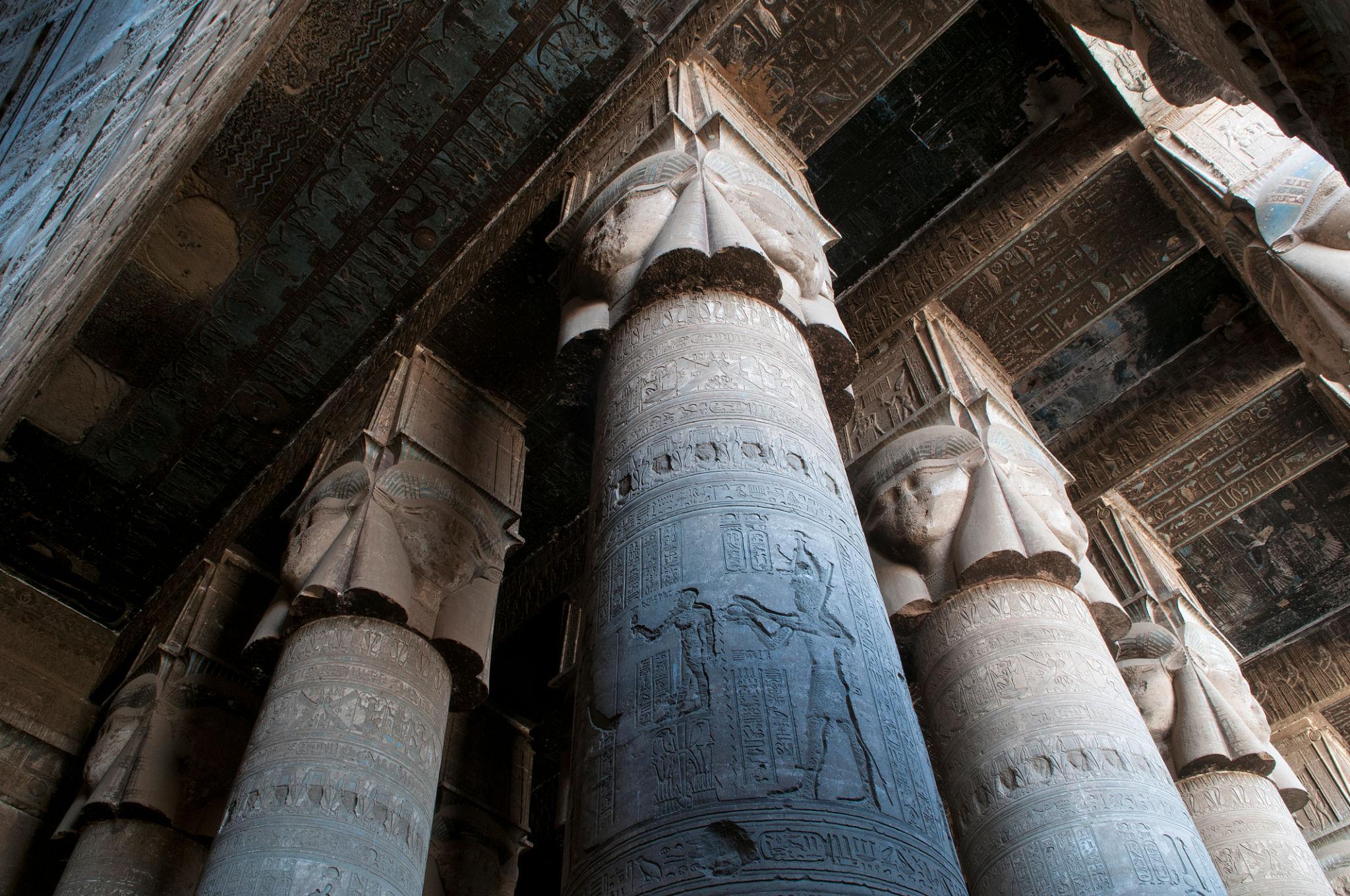 Blue-toned Hathor columns towering inside the dim hypostyle hall of Dendera.
