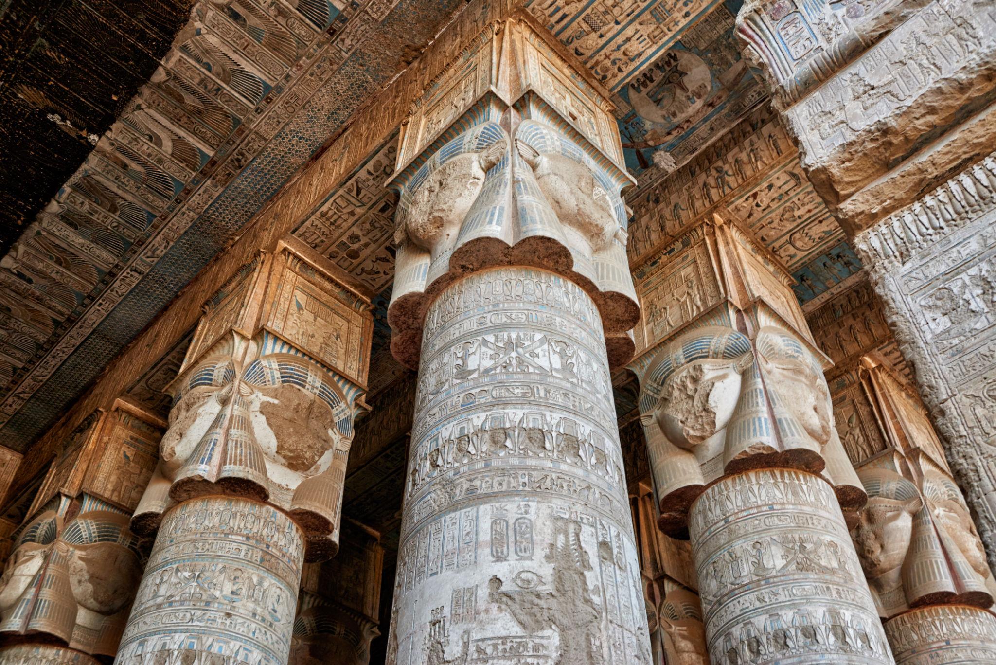 Cluster of colossal Hathor-headed columns rising in Dendera's hypostyle hall.