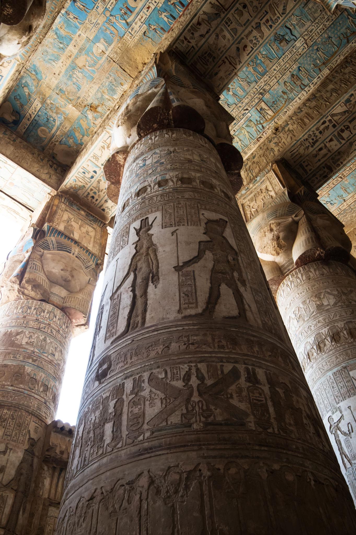 Carved column shafts with pharaoh and deity scenes beneath painted ceiling panels.