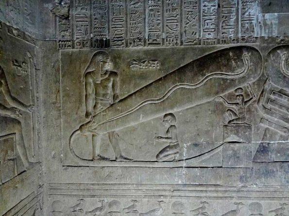 Relief of a priest and serpent figure with hieroglyphs on a Dendera temple wall.