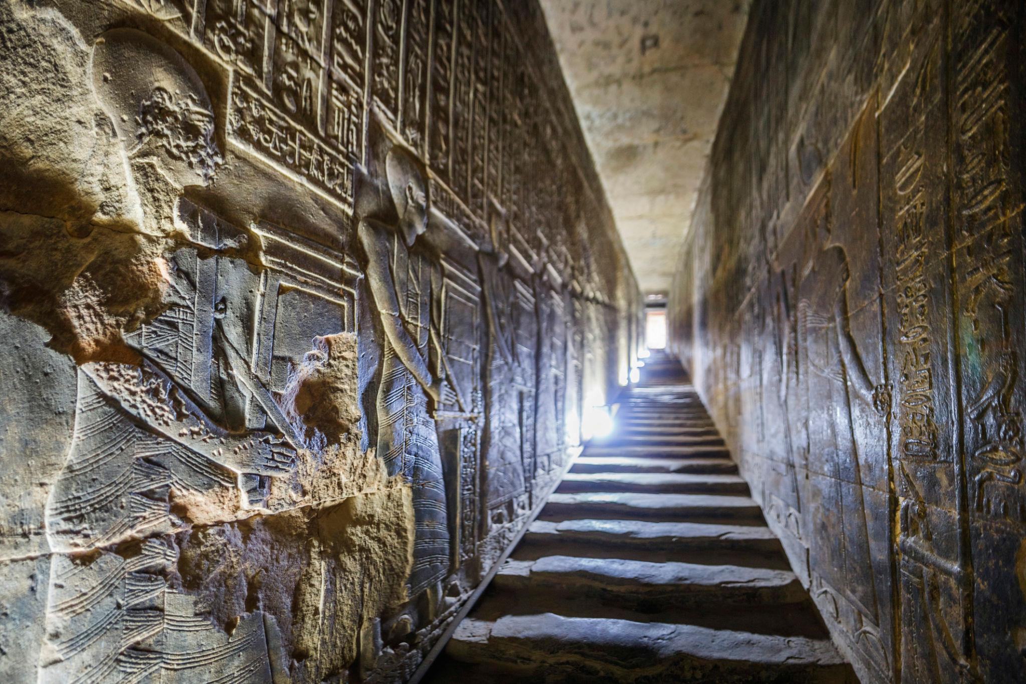 Ascending stone staircase lined with carved reliefs leading to Dendera's rooftop.