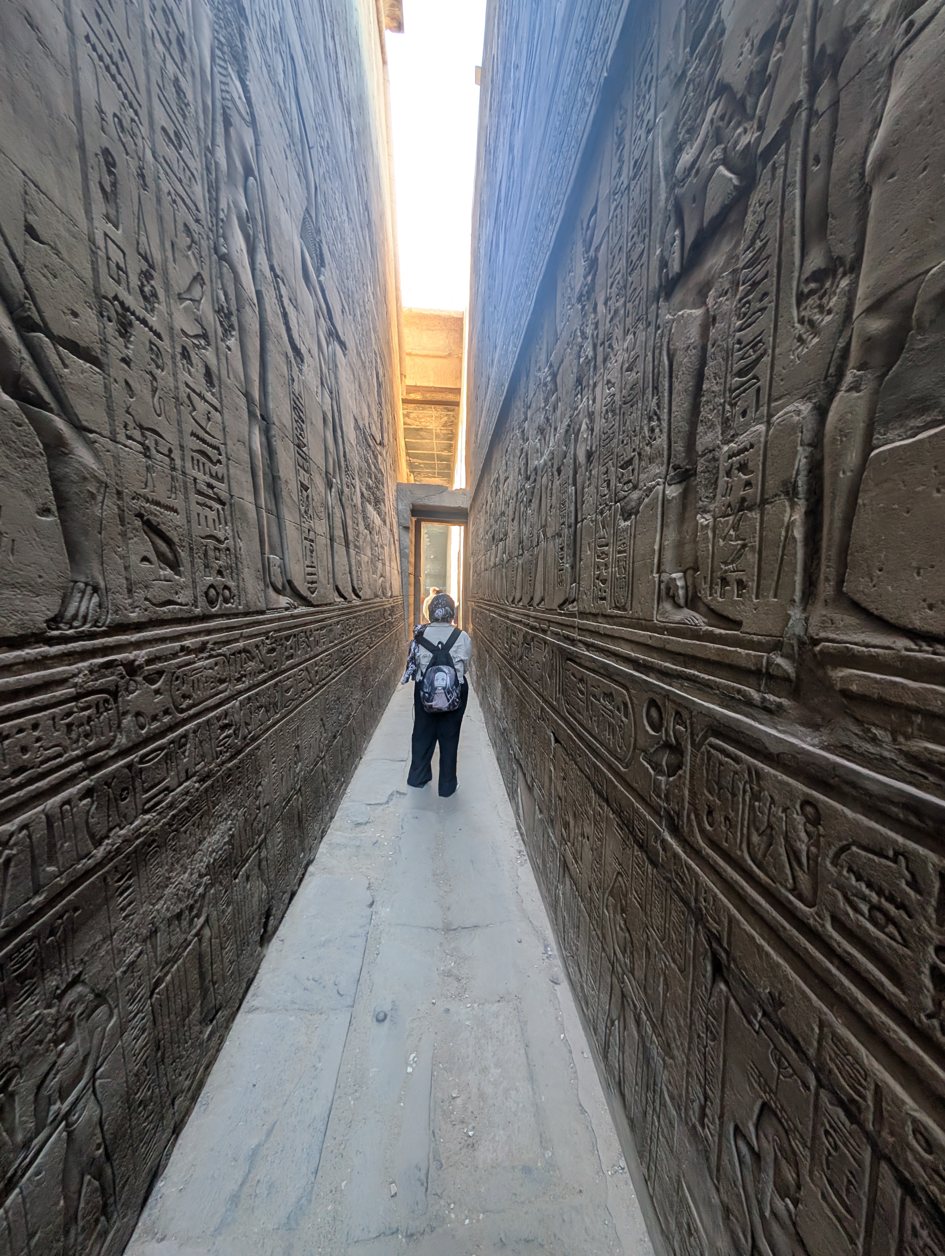 Visitor walking away down the carved ambulatory corridor at the Temple of Edfu.
