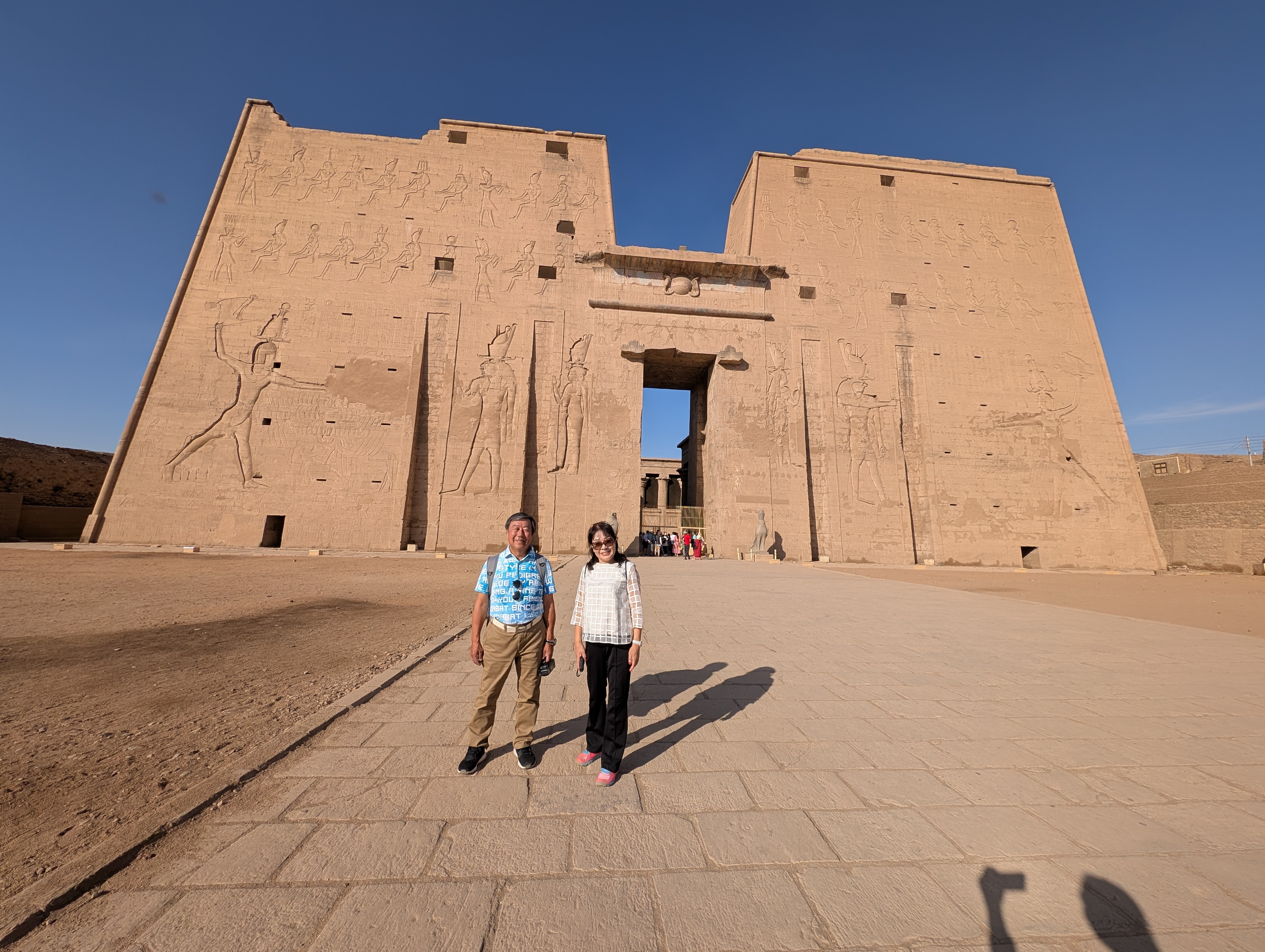 Couple posing on the plaza beneath the grand pylon of the Temple of Edfu.