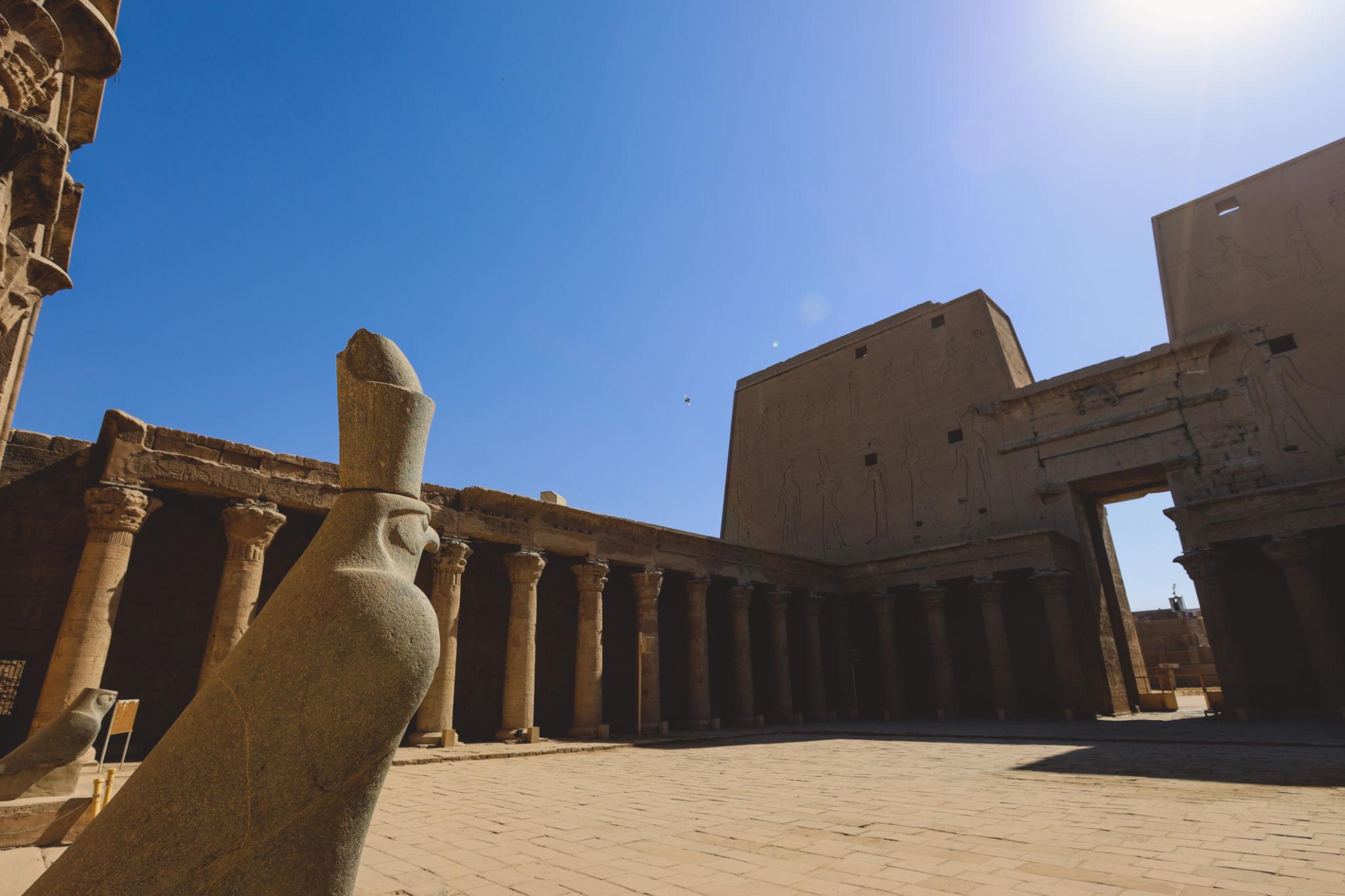 Granite Horus falcon statue in the sunlit courtyard of the Temple of Edfu.