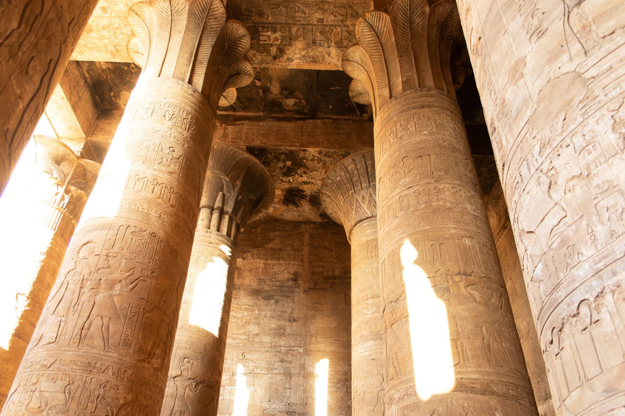 Sunlit papyrus columns inside the hypostyle hall of the Temple of Edfu.