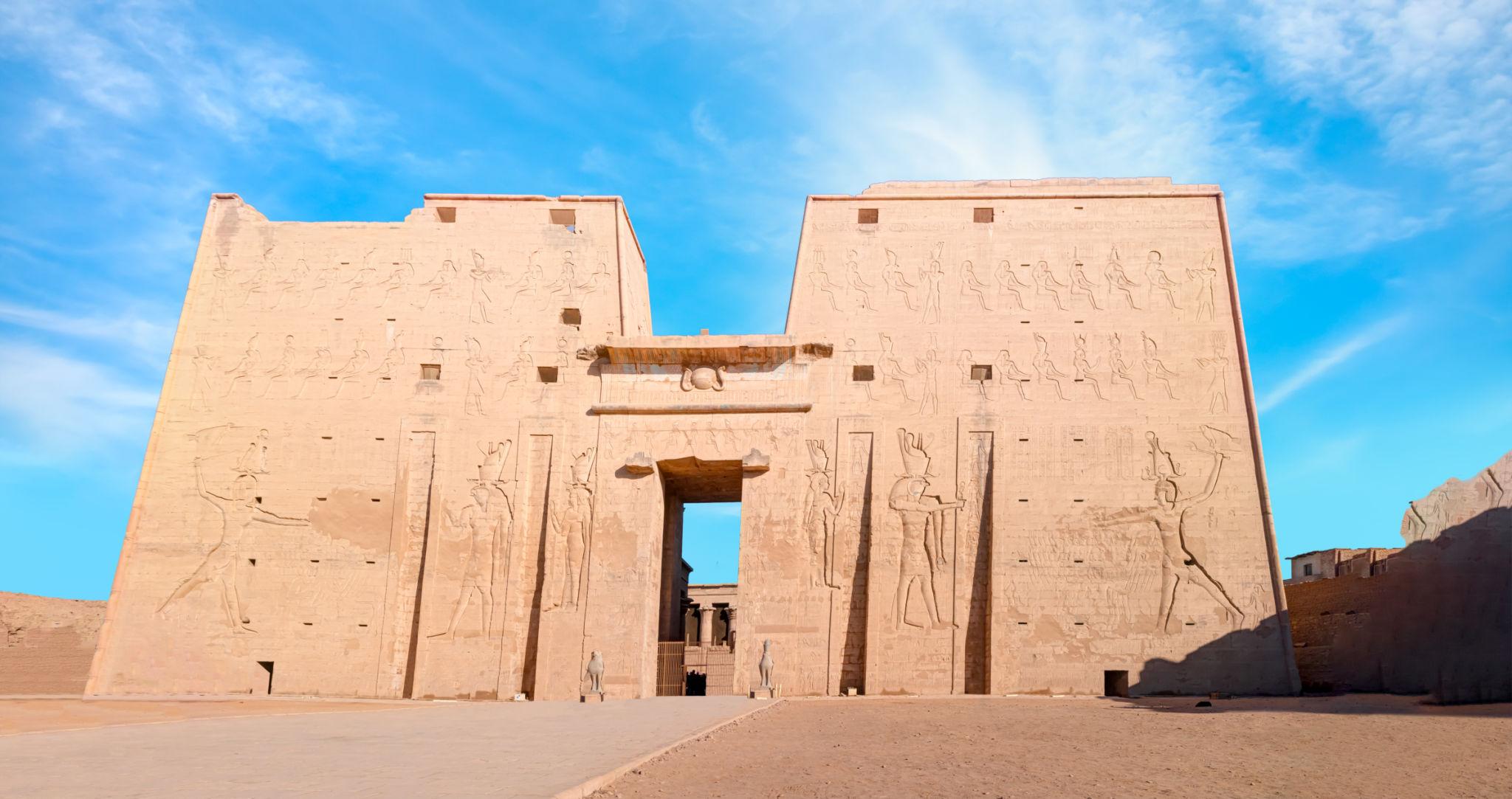 Massive first pylon facade of the Temple of Edfu against a bright blue sky.