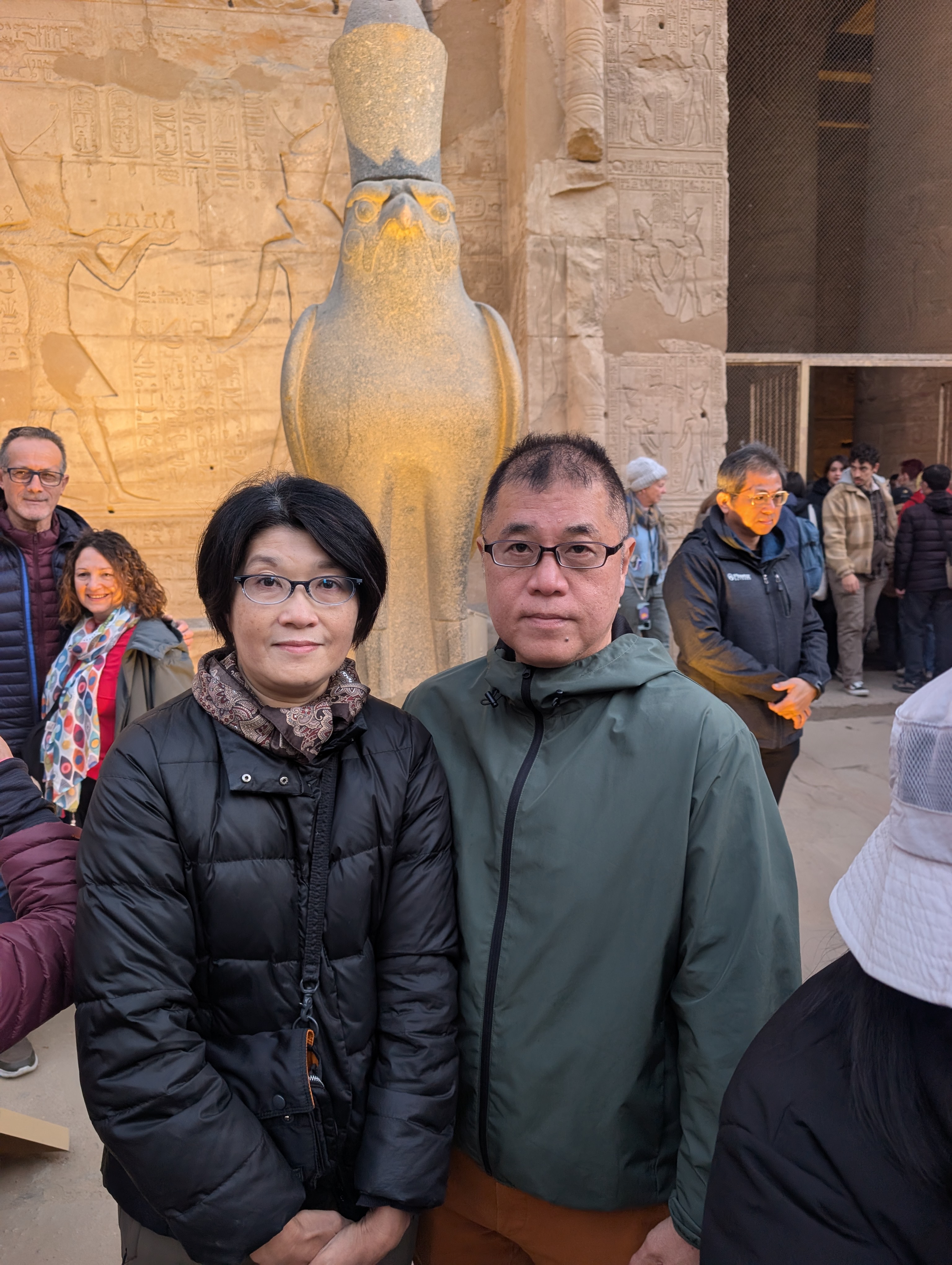 Two visitors posing beside the Horus falcon statue at the Temple of Edfu.