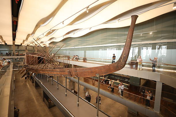 Ancient Egyptian solar boat exhibited inside a modern museum hall with visitors viewing it.