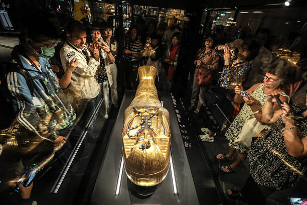 Crowds of museum visitors photograph a gleaming golden Egyptian sarcophagus in a display case.