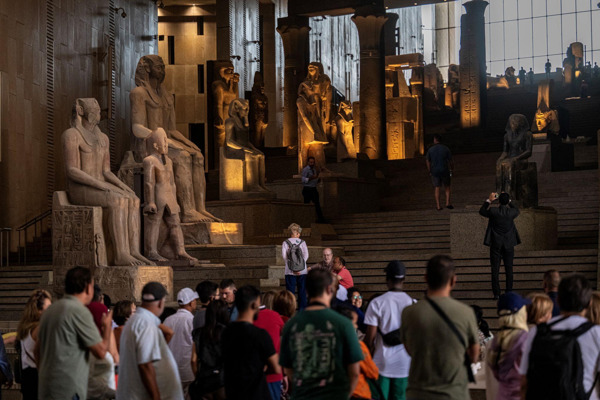 Tourists explore NMEC's grand staircase hall lined with towering ancient Egyptian pharaoh statues