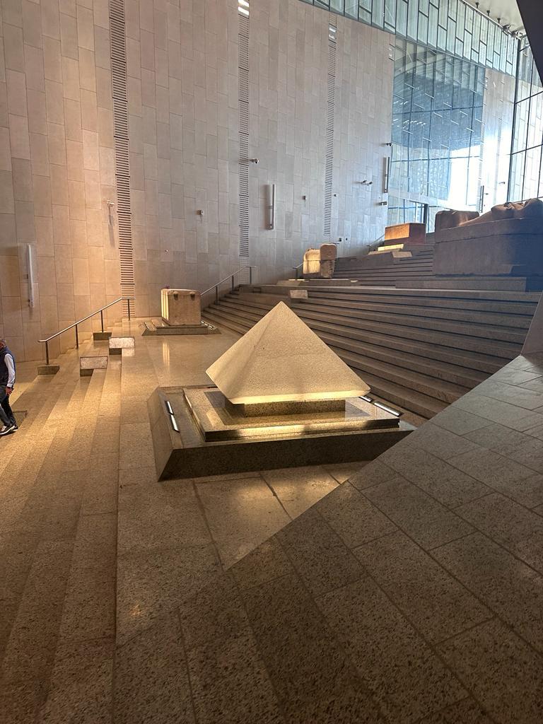 A stone pyramidion artifact on a tiered pedestal inside the NMEC's grand limestone atrium