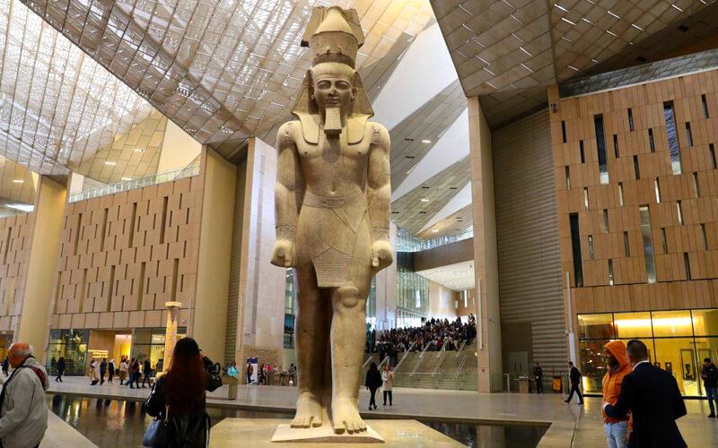 Colossal ancient Egyptian pharaoh statue standing in the modern NMEC museum atrium