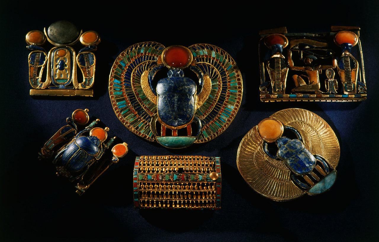 Collection of ancient Egyptian gold and gemstone scarab jewelry pieces on dark blue fabric
