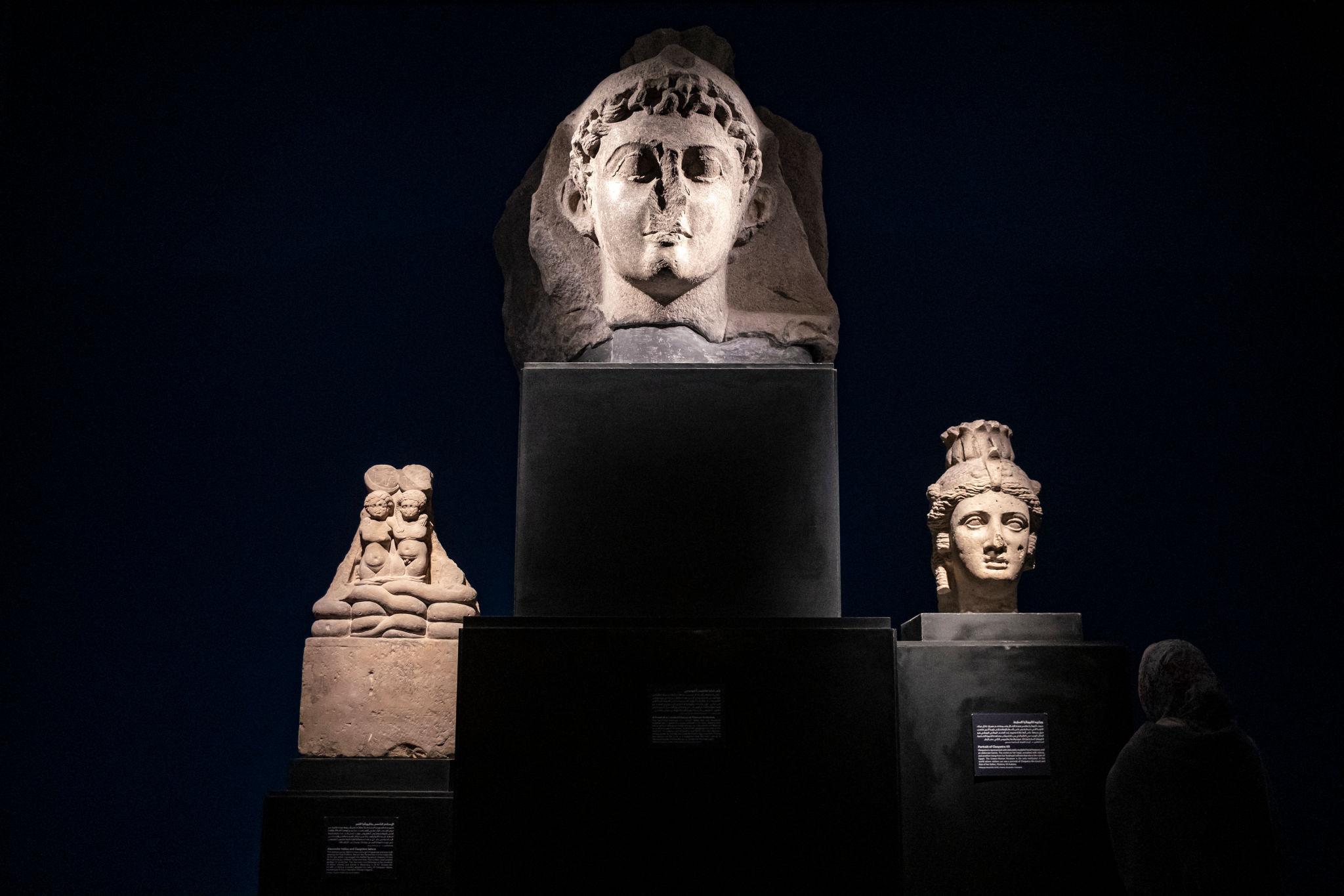 Colossal stone head and sculpted busts illuminated against deep blue museum walls