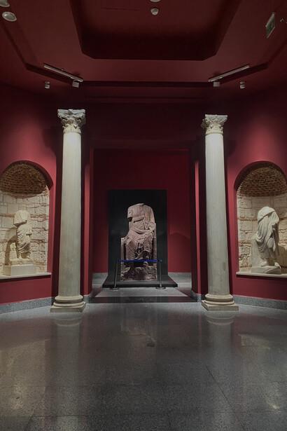 Corinthian columns framing a red-walled exhibition hall with ancient statuary