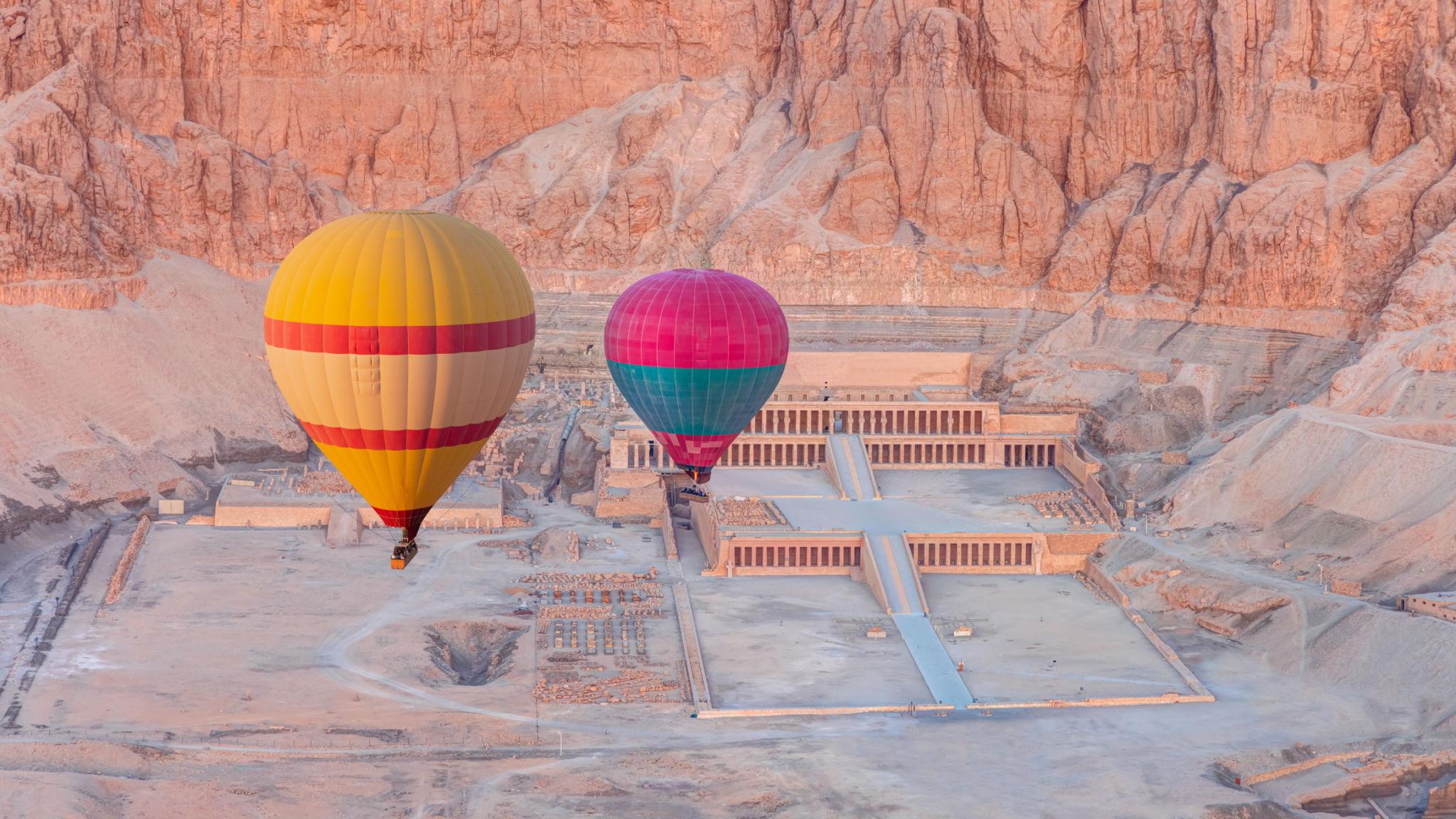 Colorful hot-air balloons drifting over Hatshepsut Temple at dawn
