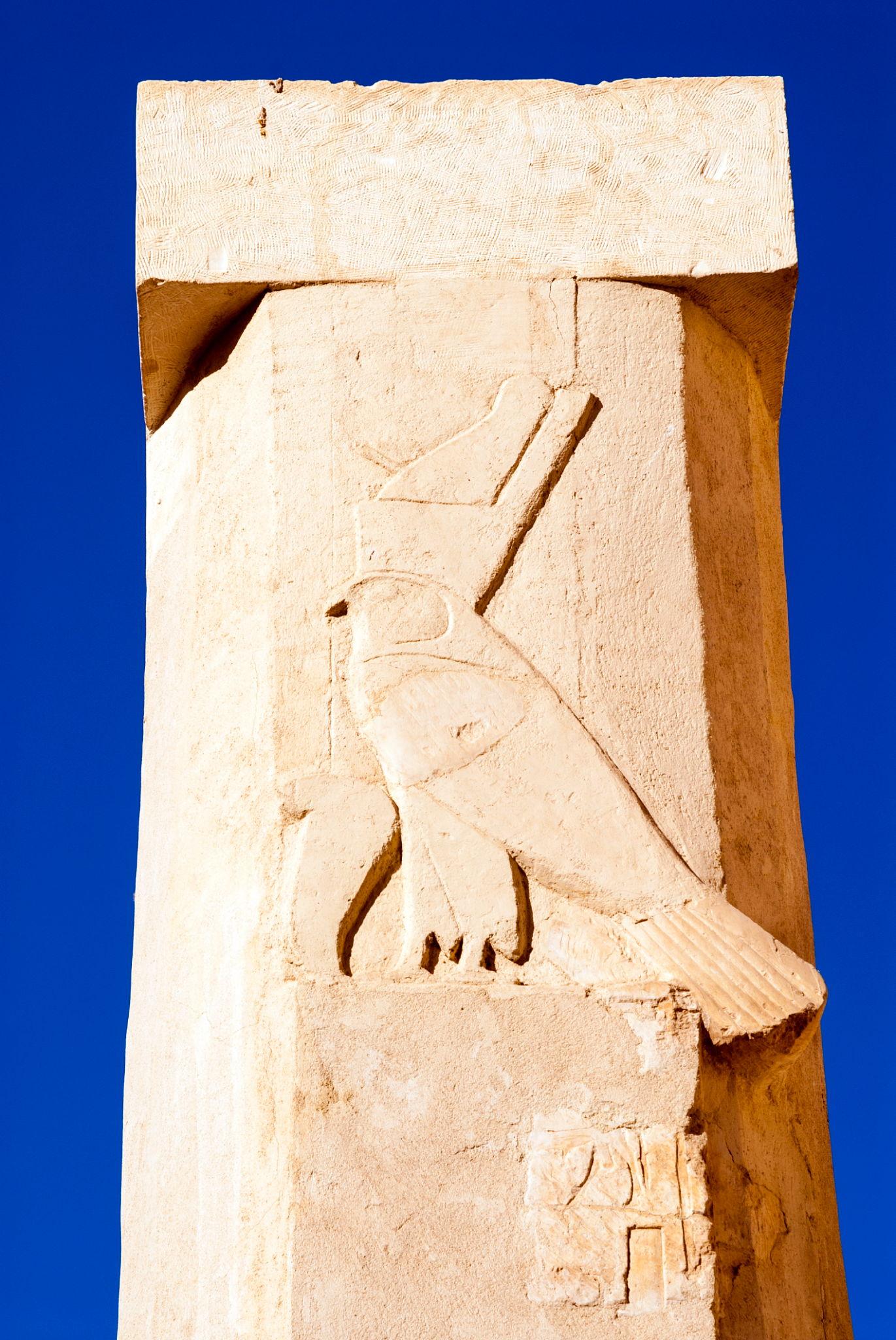 Sandstone pillar carved with hieroglyphic falcon relief against deep blue sky