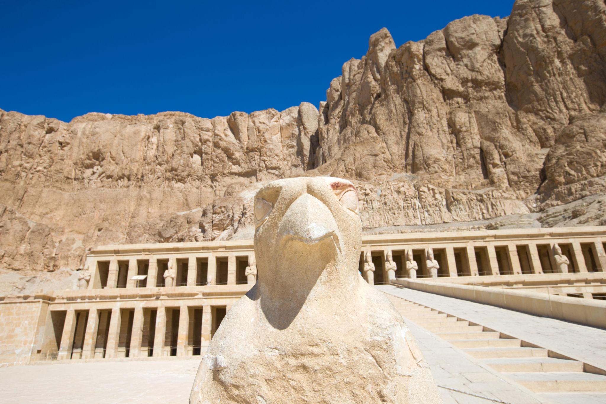 Horus falcon statue framing Hatshepsut Temple colonnade and Deir el-Bahari cliffs